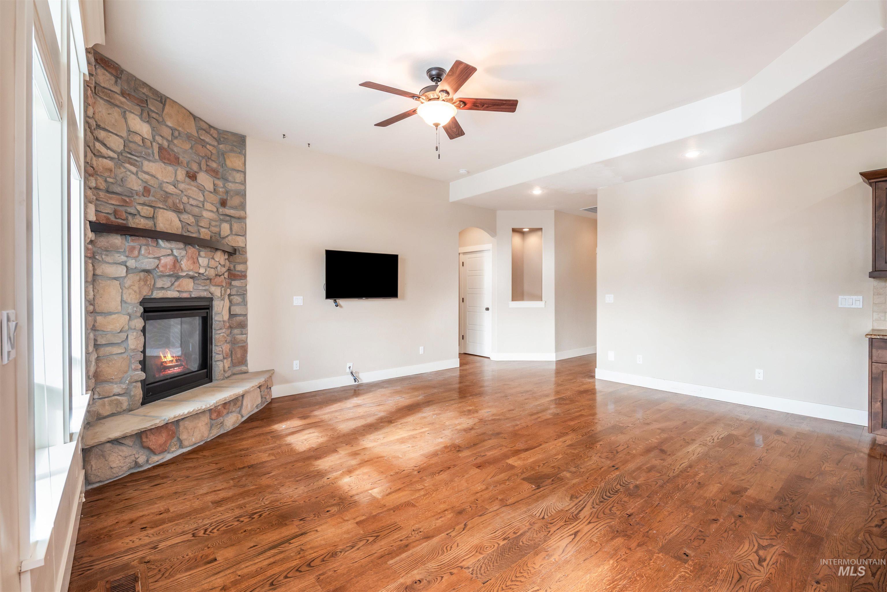 Unfurnished living room with a fireplace, arched walkways, wood finished floors, ceiling fan, and recessed lighting