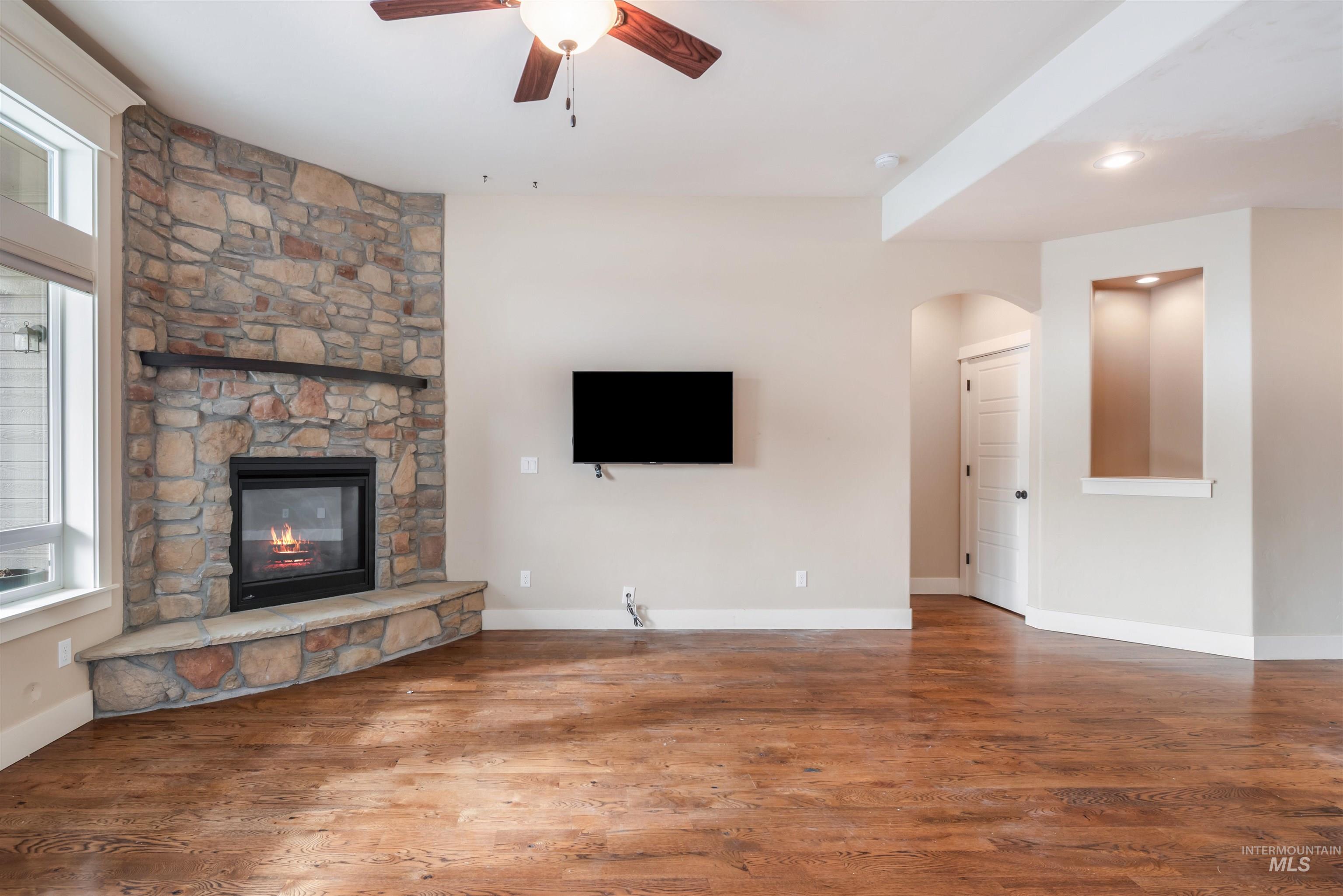 Unfurnished living room featuring arched walkways, wood finished floors, a ceiling fan, and a fireplace