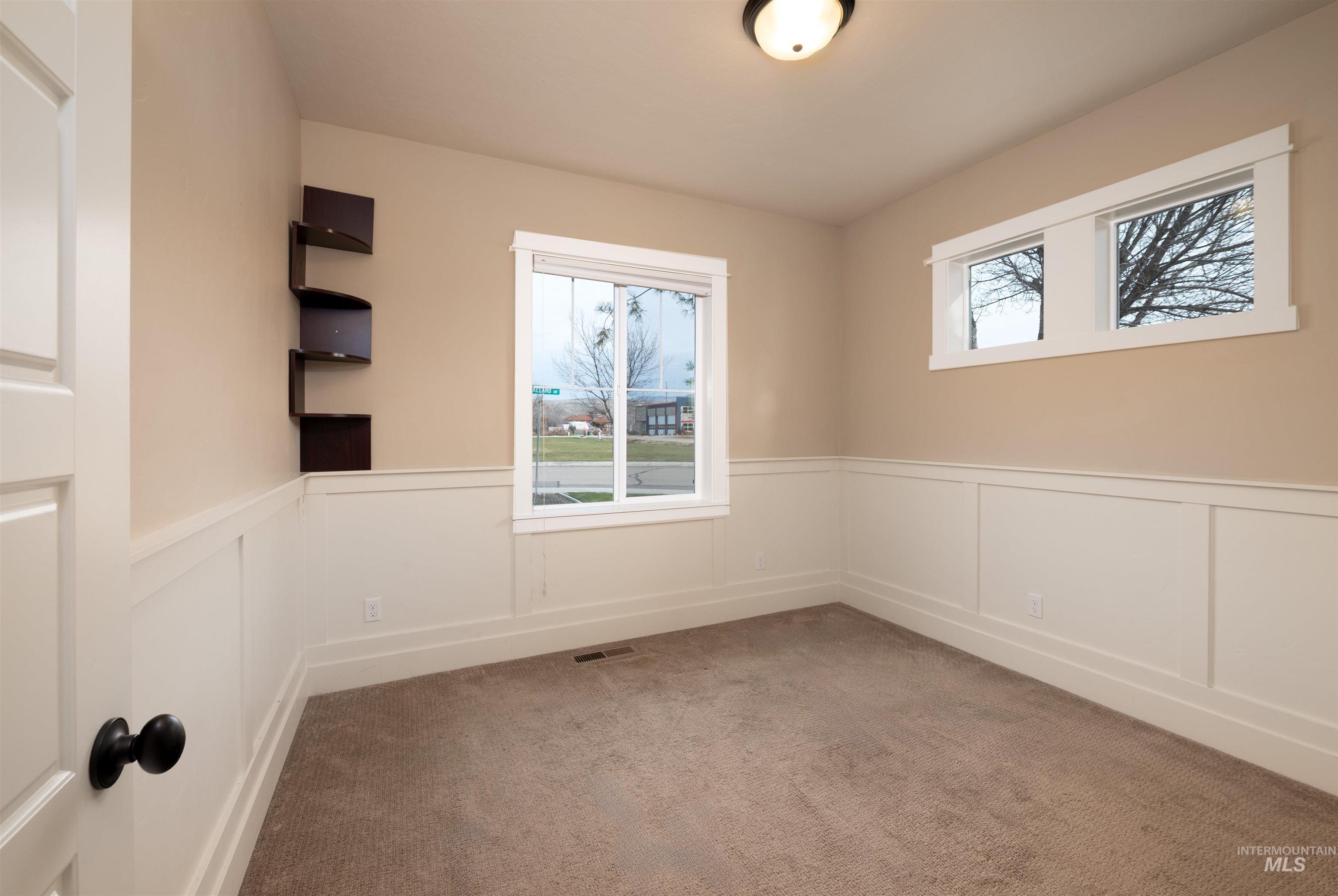 Empty room with a wainscoted wall, a decorative wall, and light colored carpet