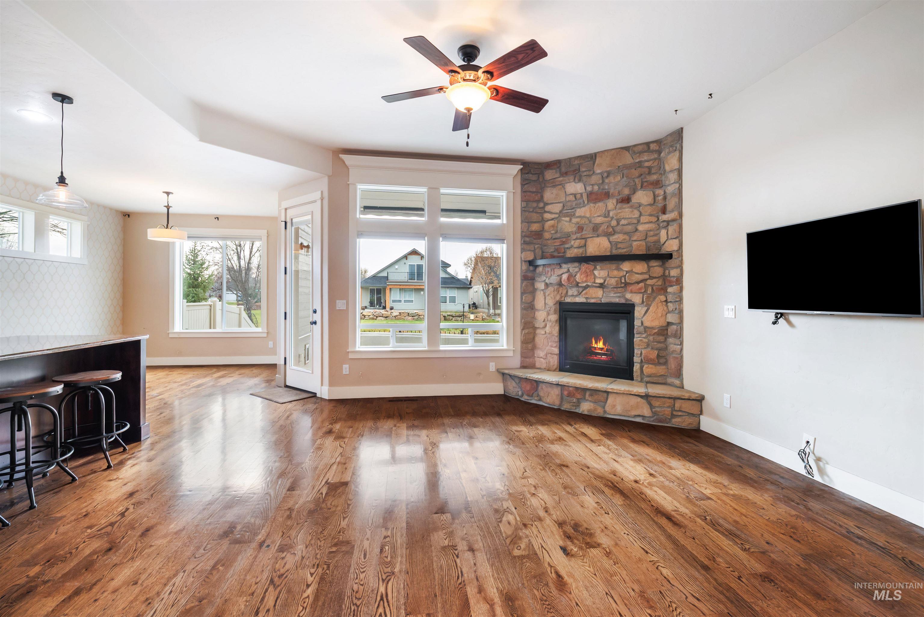 Unfurnished living room featuring wood finished floors, a stone fireplace, ceiling fan, and healthy amount of natural light