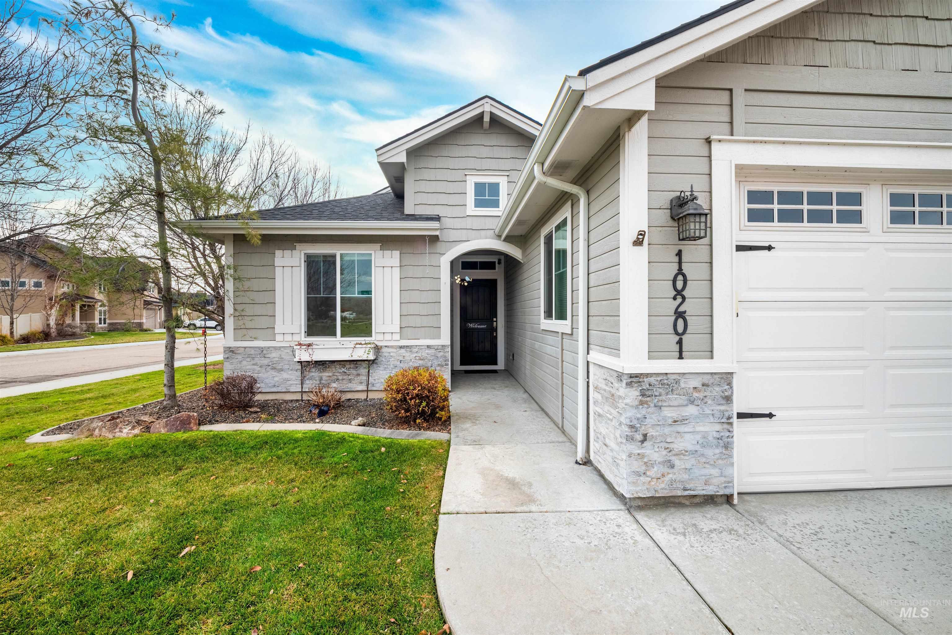 View of front of home featuring stone siding, a front lawn, roof with shingles, and an attached garage