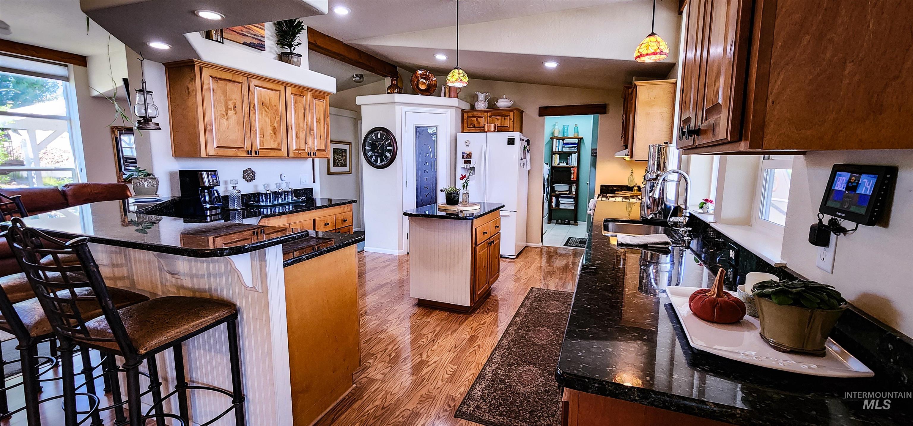 Kitchen with light wood-style floors, brown cabinets, lofted ceiling, a center island, and dark stone counters