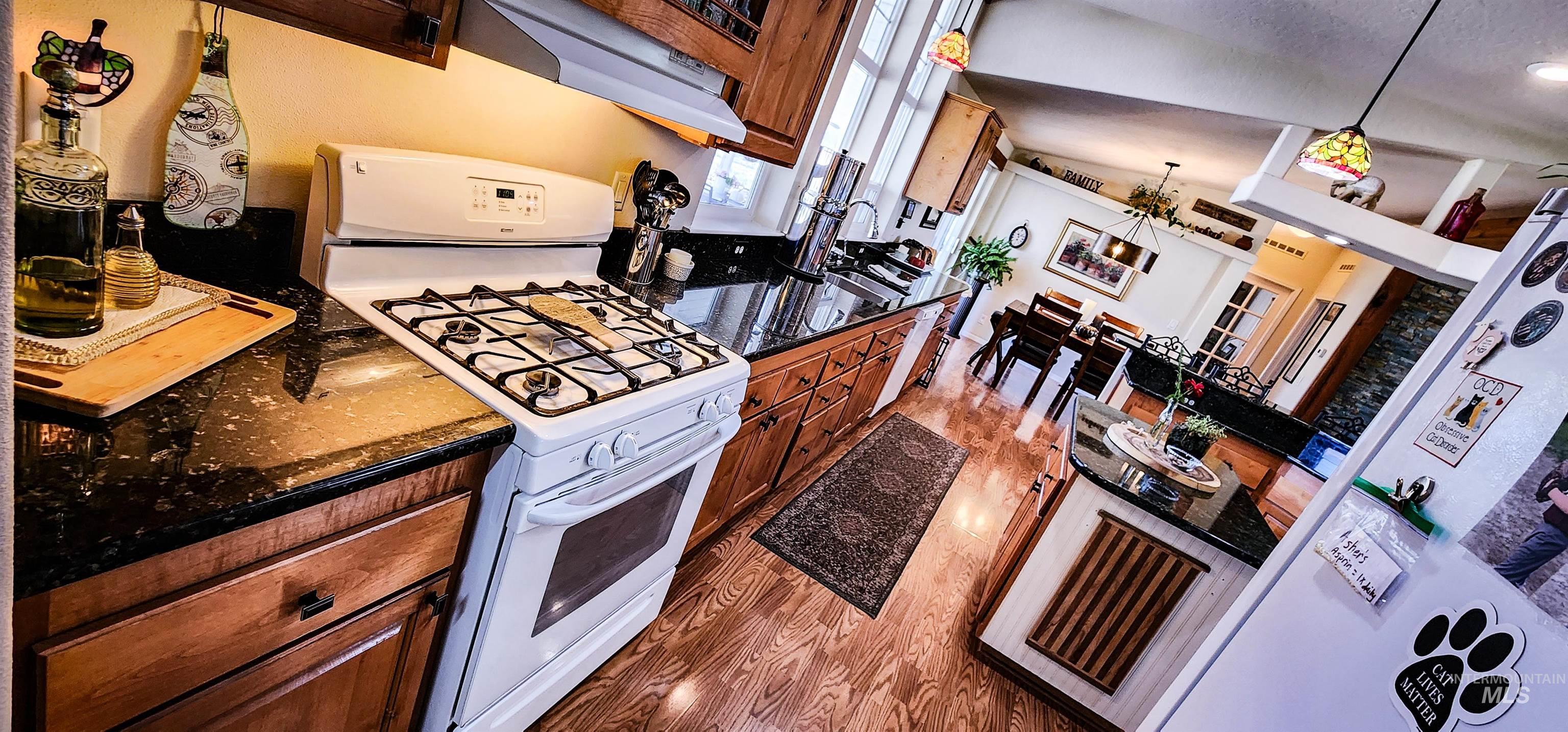Kitchen featuring gas range gas stove, dark wood-type flooring, ventilation hood, decorative light fixtures, and brown cabinets