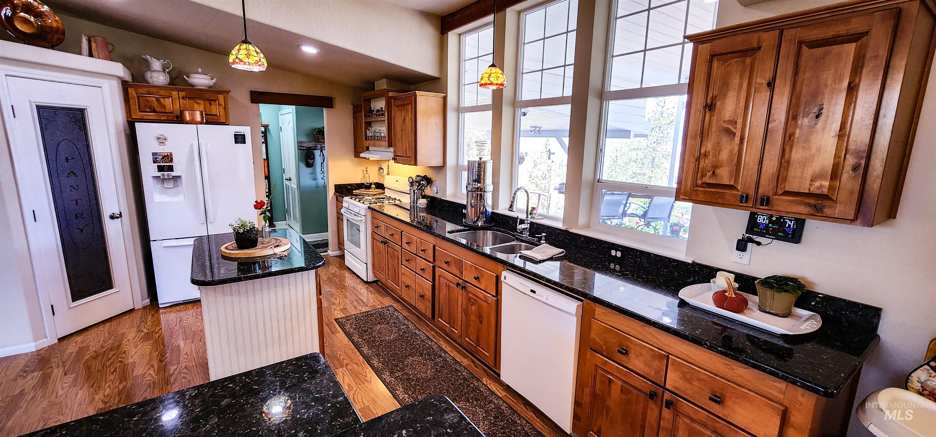 Kitchen featuring brown cabinetry, white appliances, dark stone countertops, light wood finished floors, and lofted ceiling