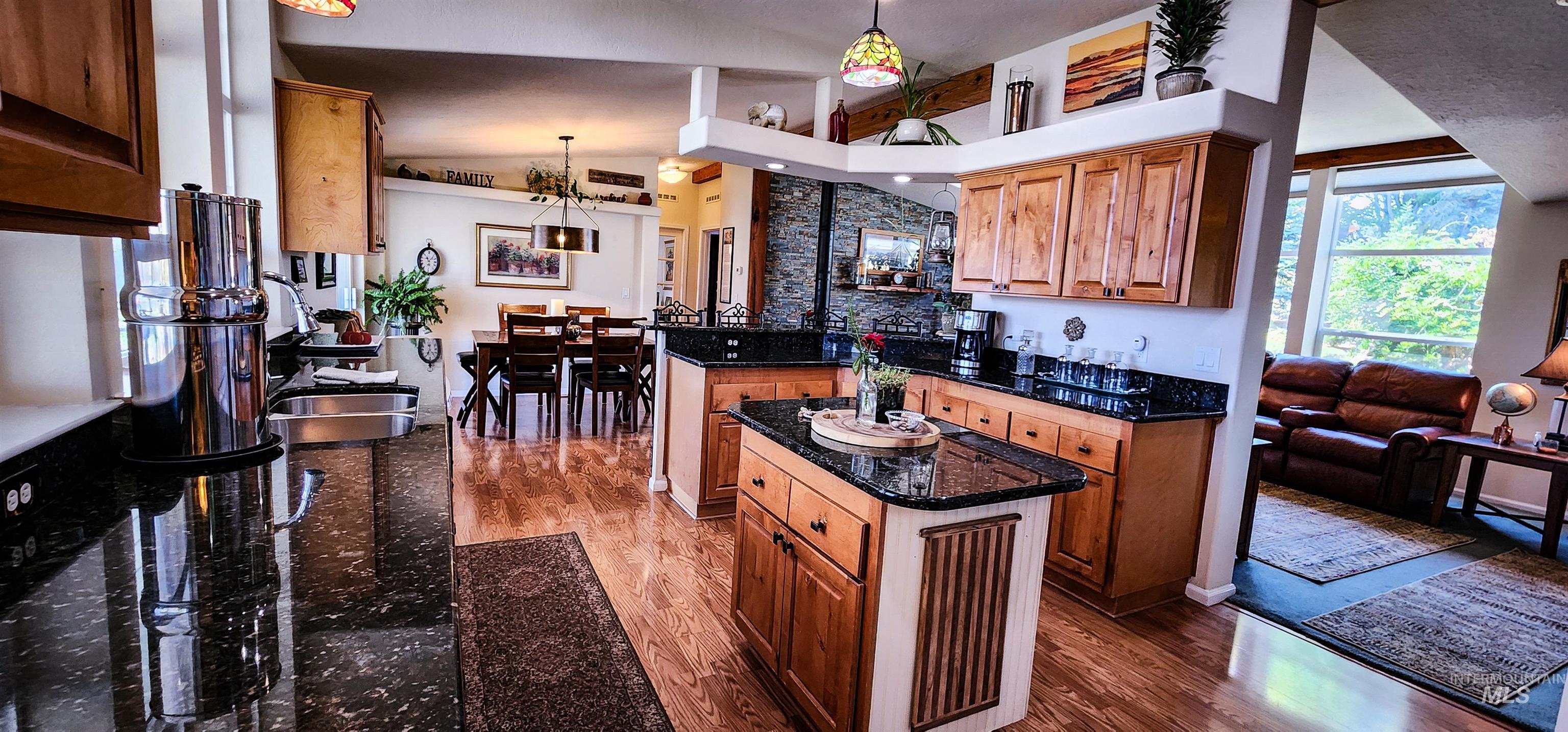 Kitchen featuring dark wood-style flooring, brown cabinets, a center island, dark stone counters, and pendant lighting