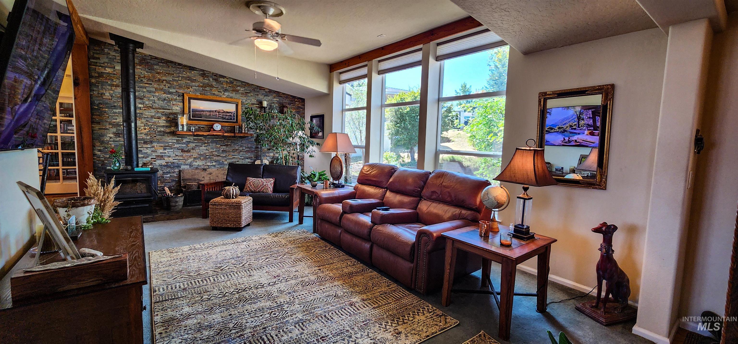Living room featuring a wood stove, ceiling fan, lofted ceiling, and carpet flooring