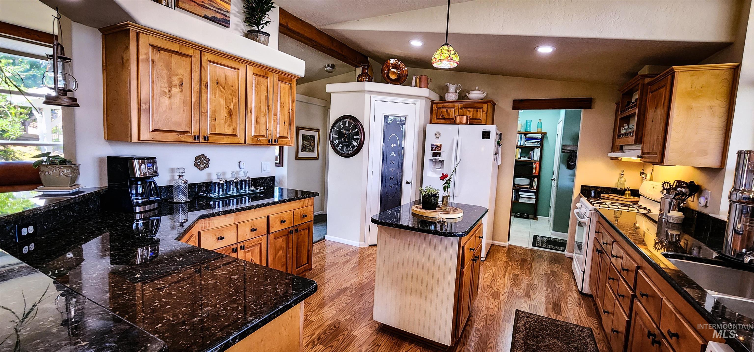 Kitchen with decorative light fixtures, brown cabinets, dark wood-type flooring, white appliances, and vaulted ceiling