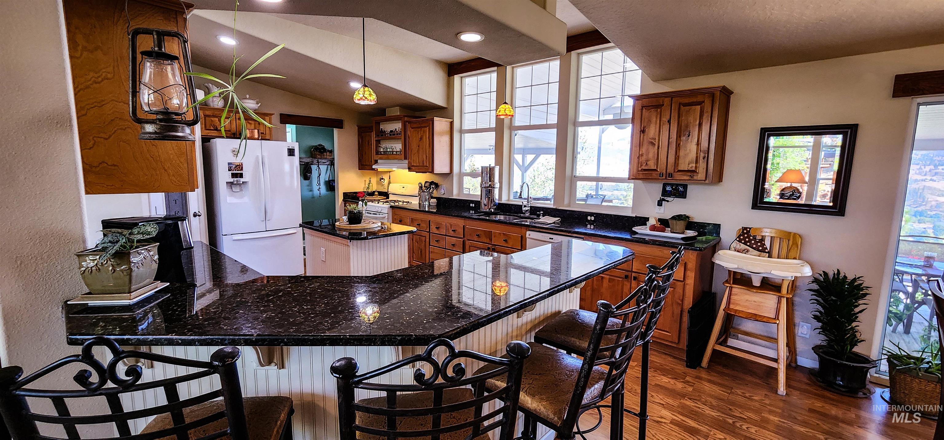 Kitchen with white appliances, decorative light fixtures, a peninsula, dark wood finished floors, and a breakfast bar area