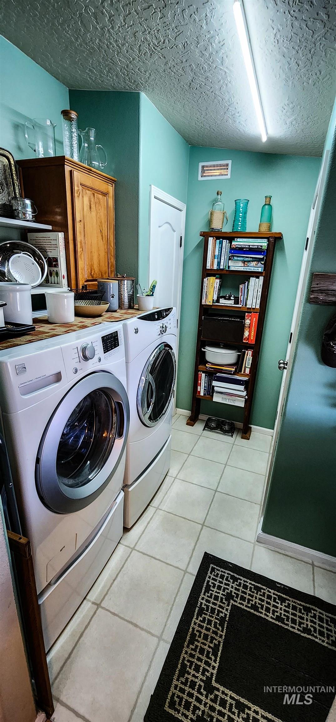 Laundry room with light tile patterned floors, a textured ceiling, washer and dryer, and cabinet space