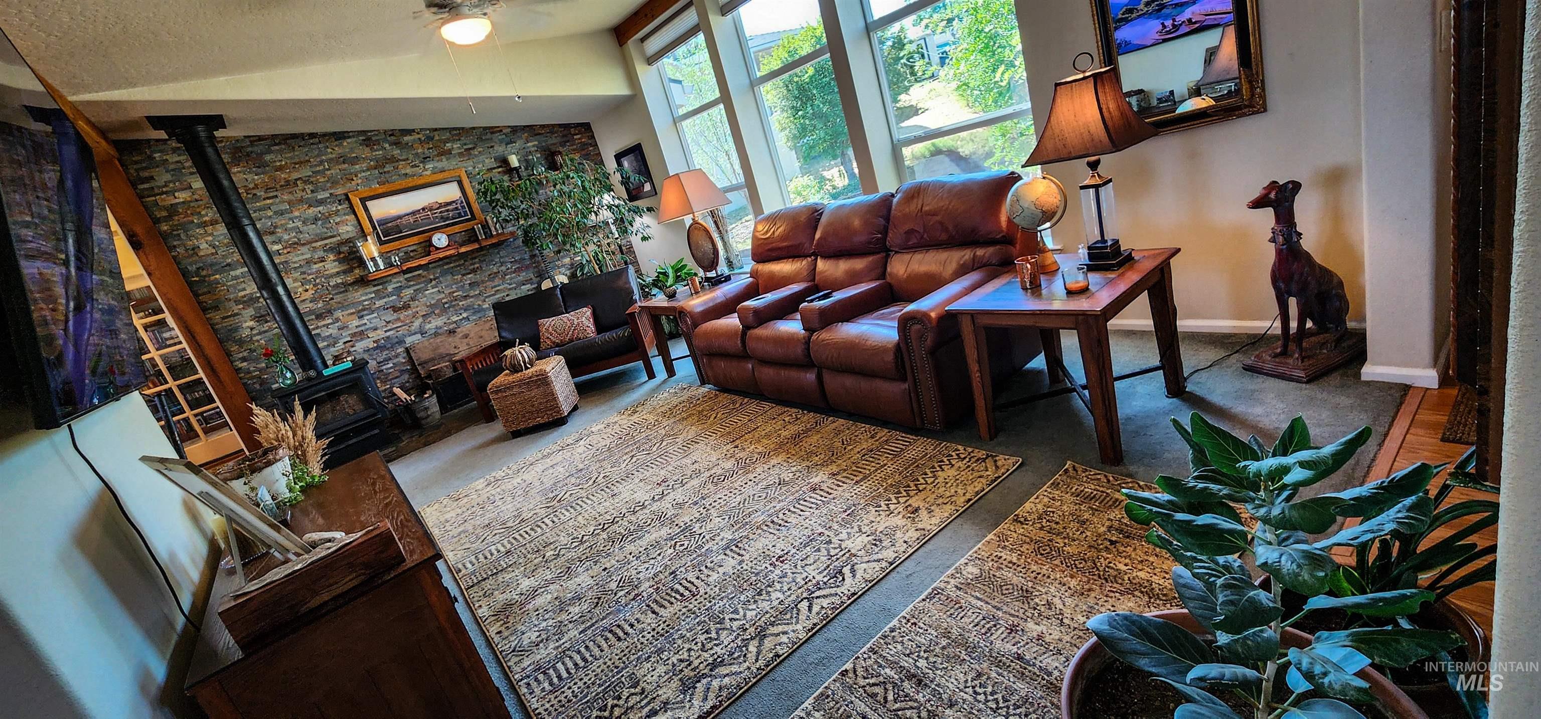 Living room with a wood stove, vaulted ceiling, a ceiling fan, and a textured ceiling
