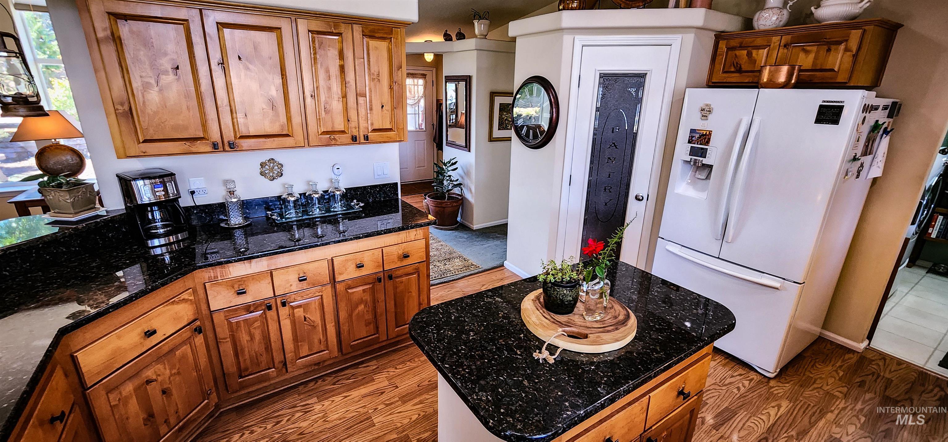 Kitchen with brown cabinets, light wood-style flooring, and white fridge with ice dispenser