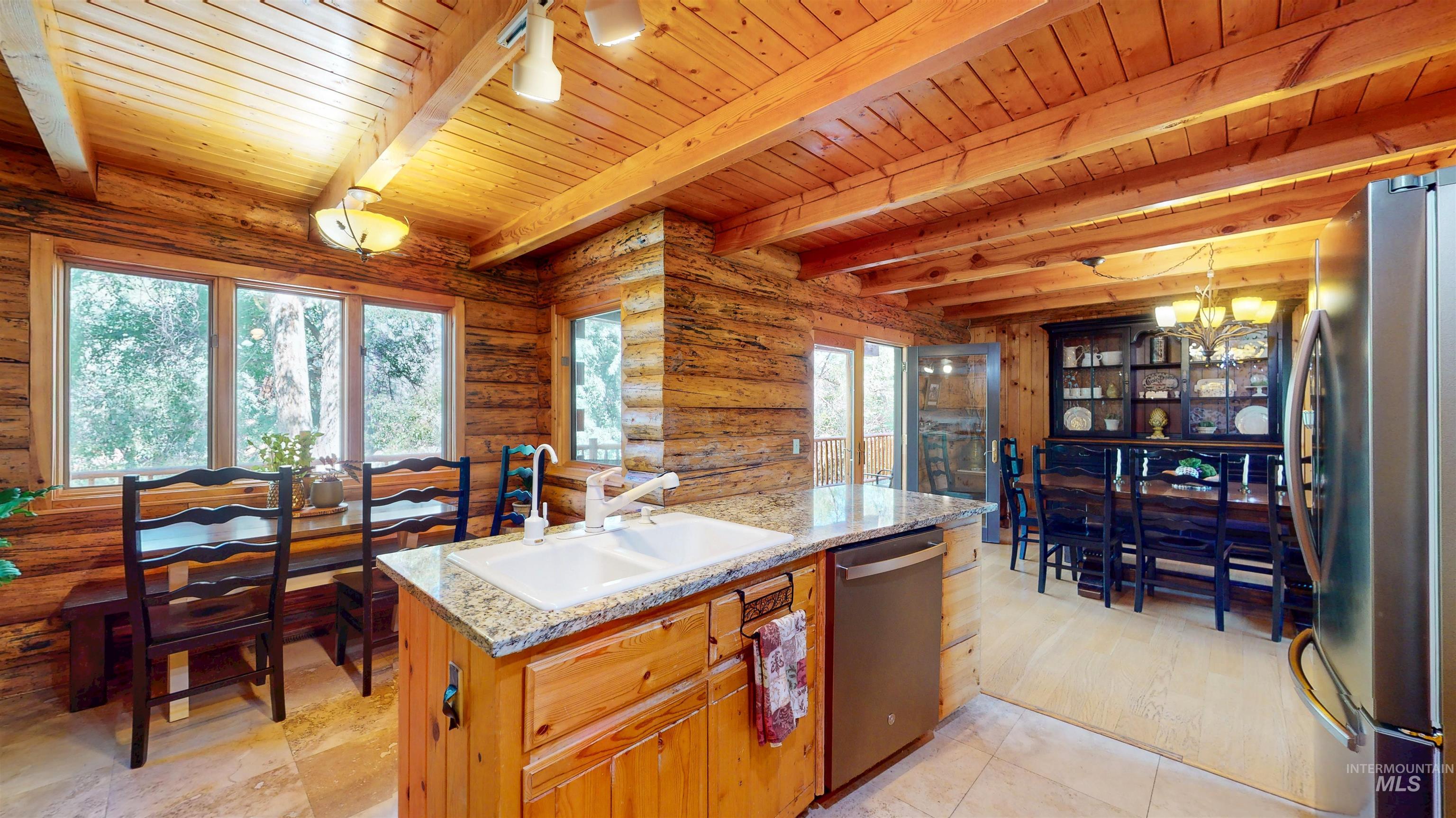 Kitchen featuring appliances with stainless steel finishes, a wooden ceiling with exposed beams, a chandelier, light stone countertops, and log walls
