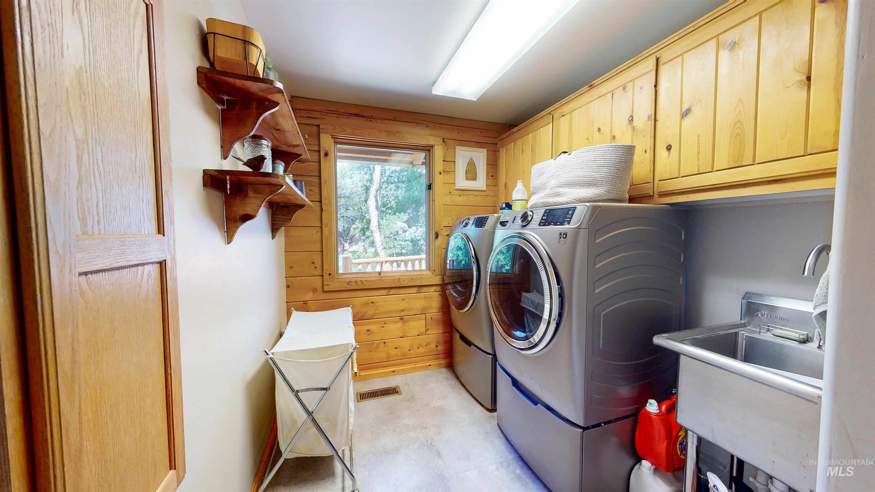 Washroom with cabinet space, washing machine and dryer, and wood walls