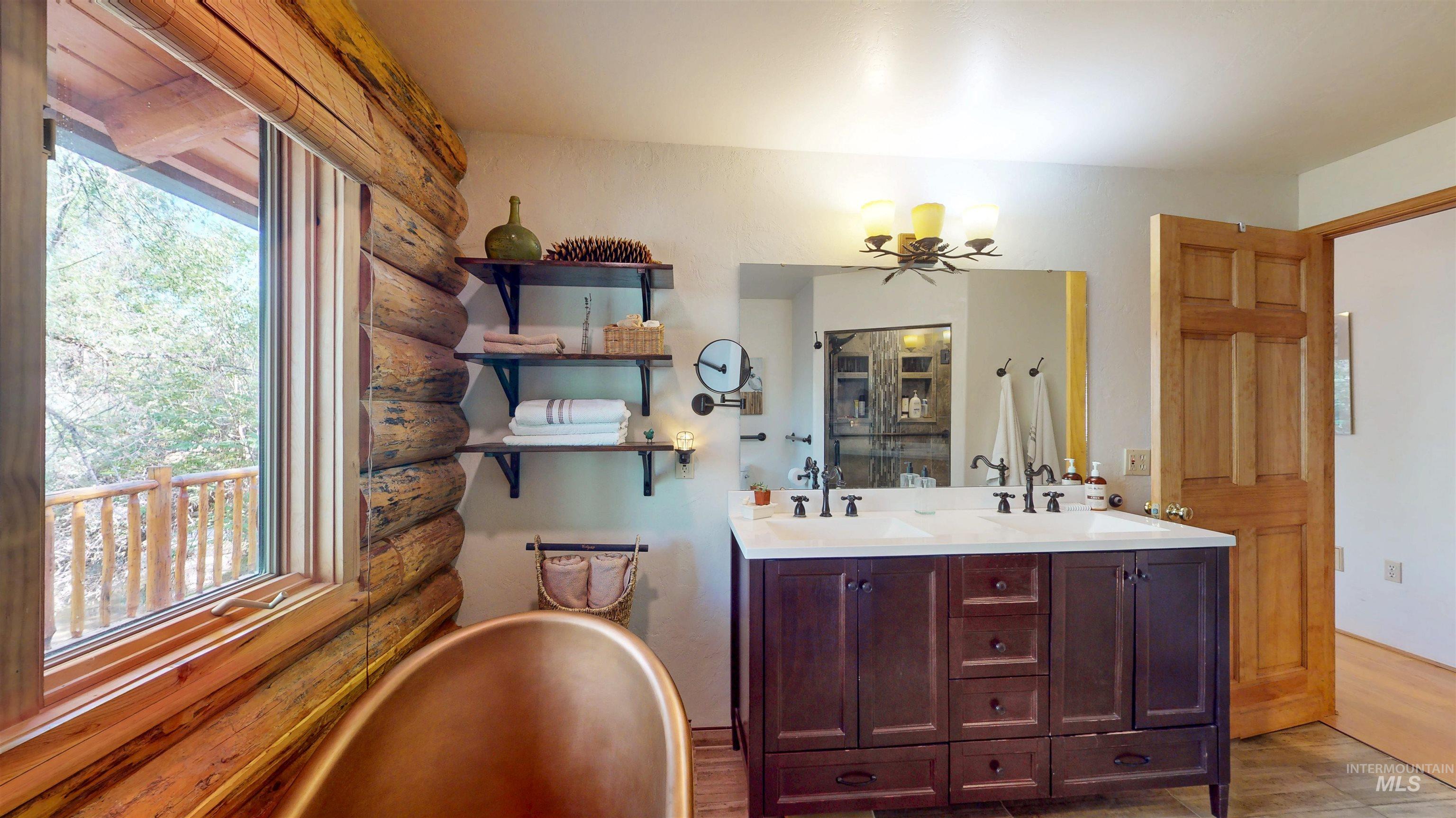 Full bathroom with healthy amount of natural light, a soaking tub, double vanity, rustic walls, and wood finished floors