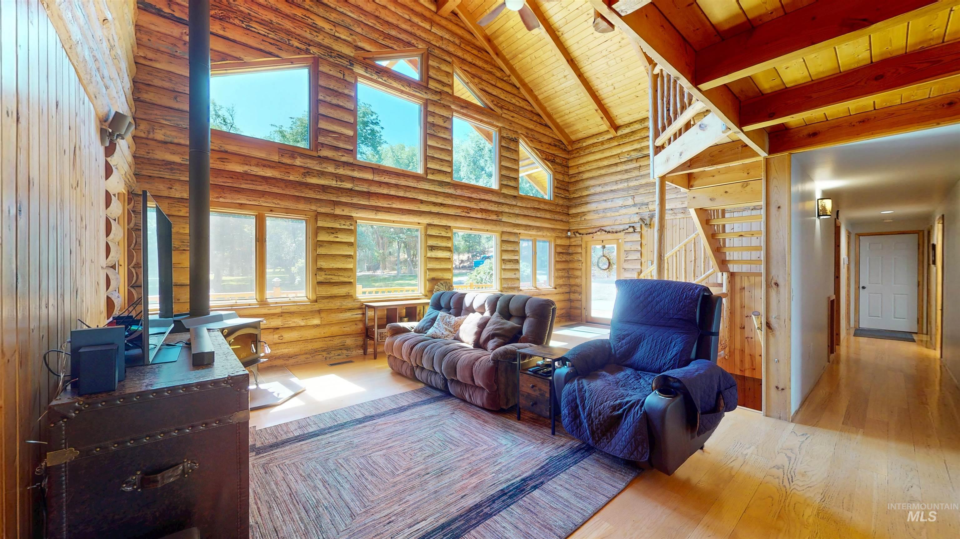Living area with high vaulted ceiling, wood finished floors, a wood ceiling with exposed beams, and log walls