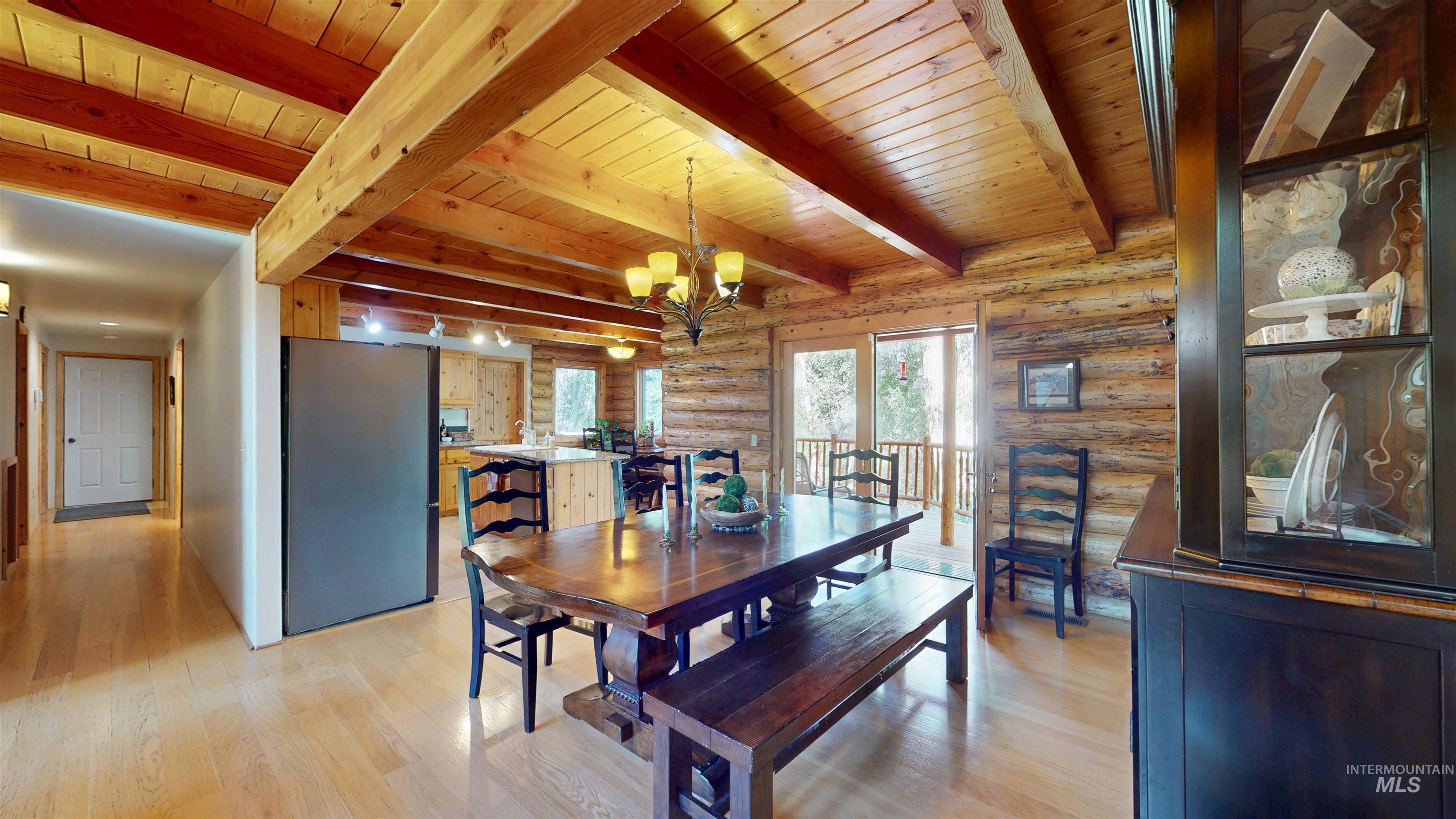 Dining room featuring rustic walls, light wood finished floors, a chandelier, and a wood ceiling with exposed beams