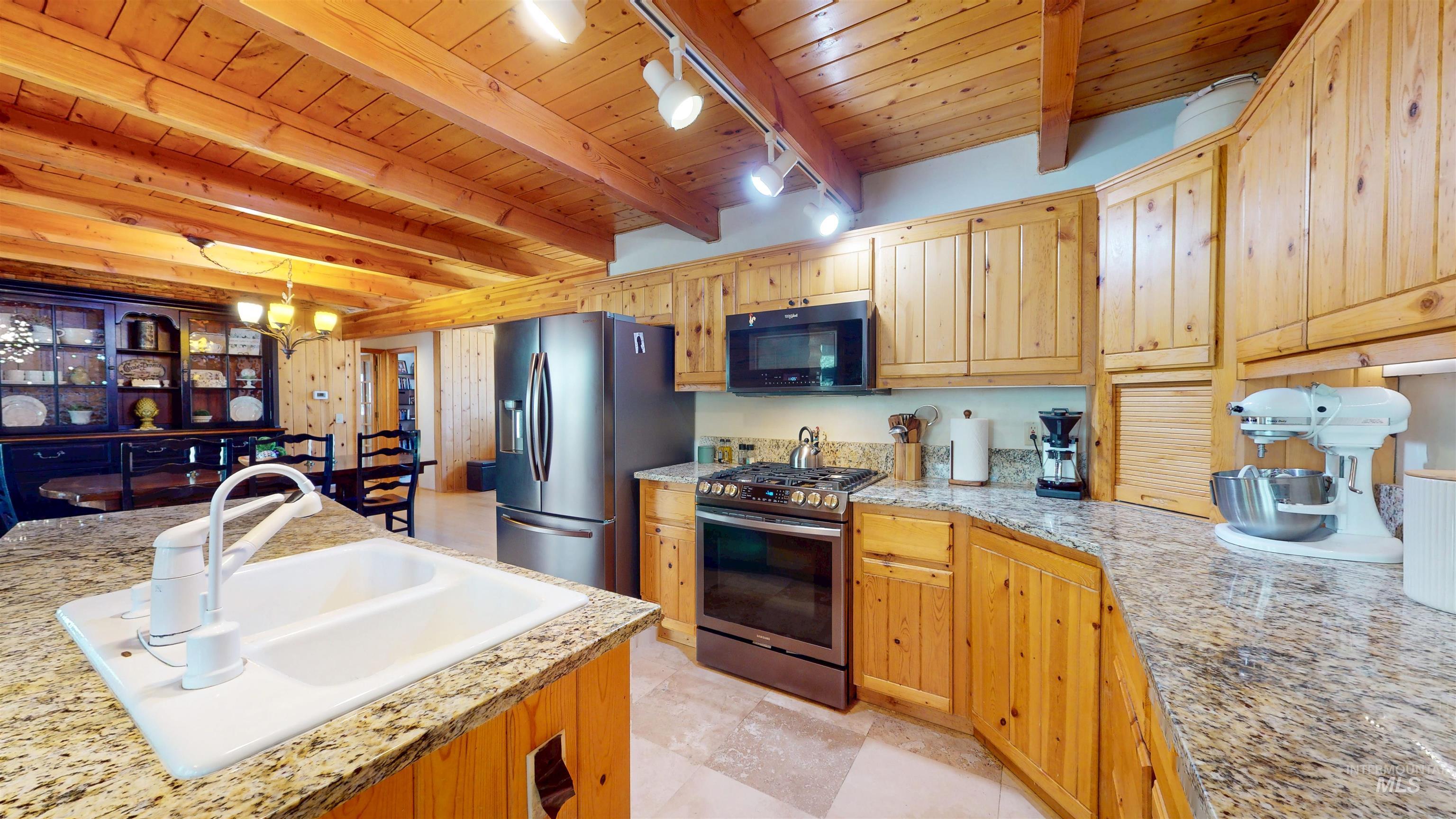 Kitchen with stainless steel appliances, a wood ceiling with exposed beams, a chandelier, track lighting, and decorative light fixtures