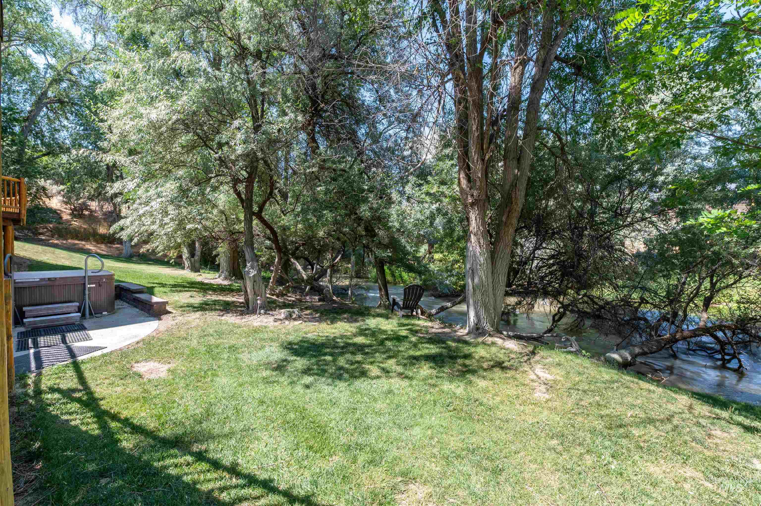 View of green lawn with a hot tub and view of wooded area