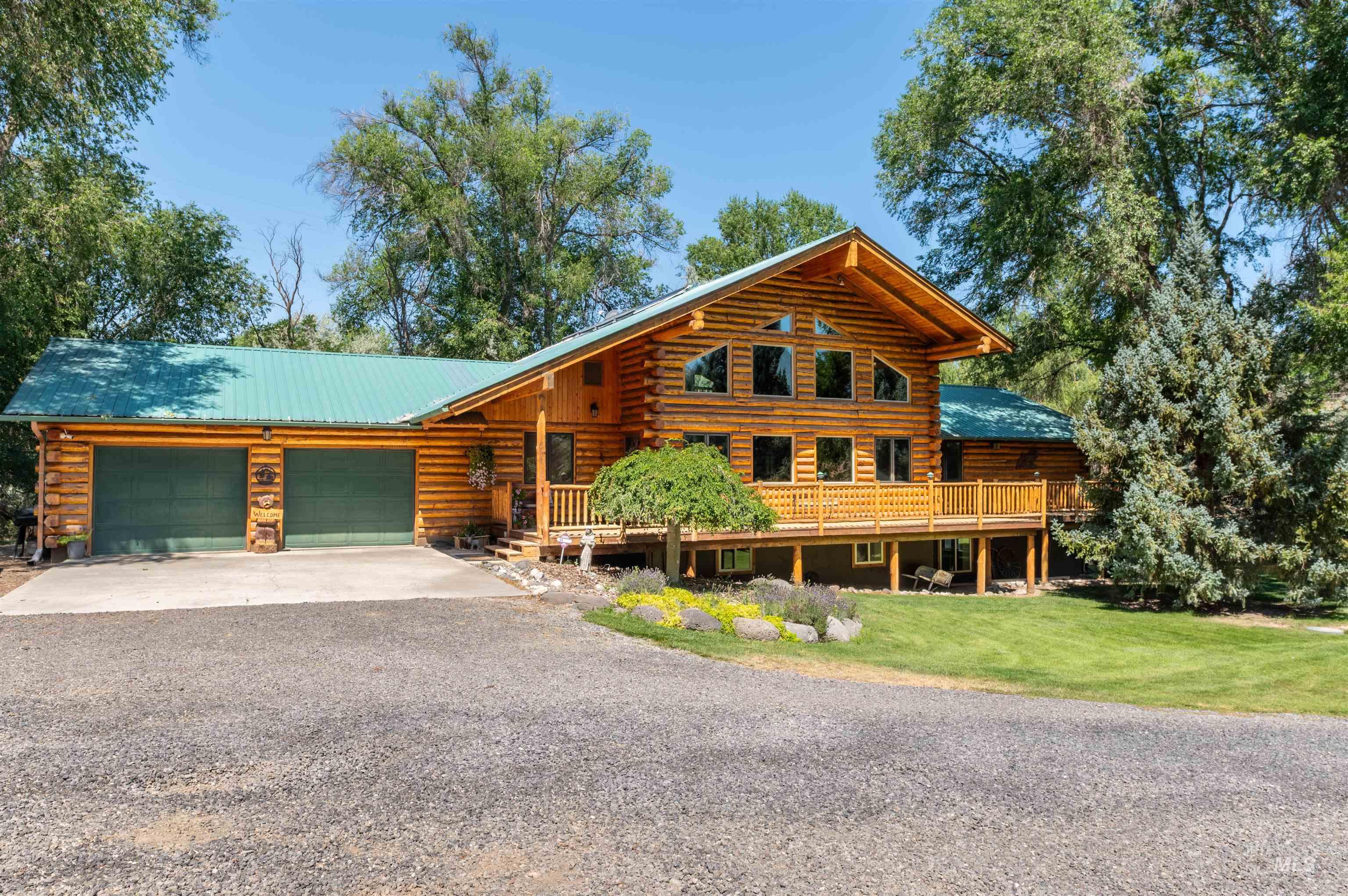 Cabin featuring log exterior, gravel driveway, an attached garage, a front lawn, and a metal roof