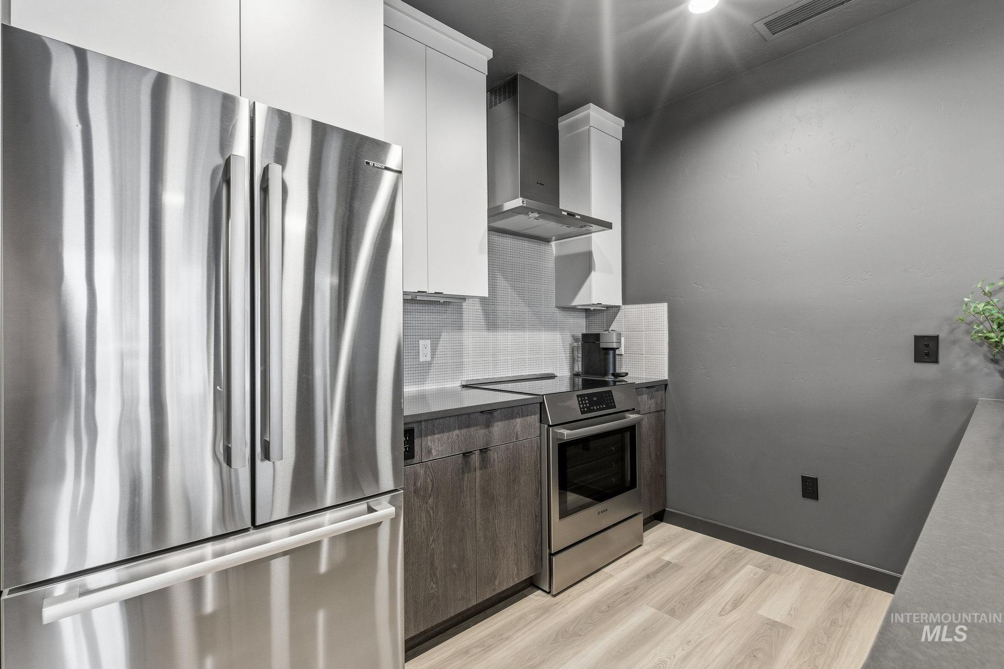 Kitchen with stainless steel appliances, modern cabinets, light wood finished floors, dual tone cabinets, and backsplash
