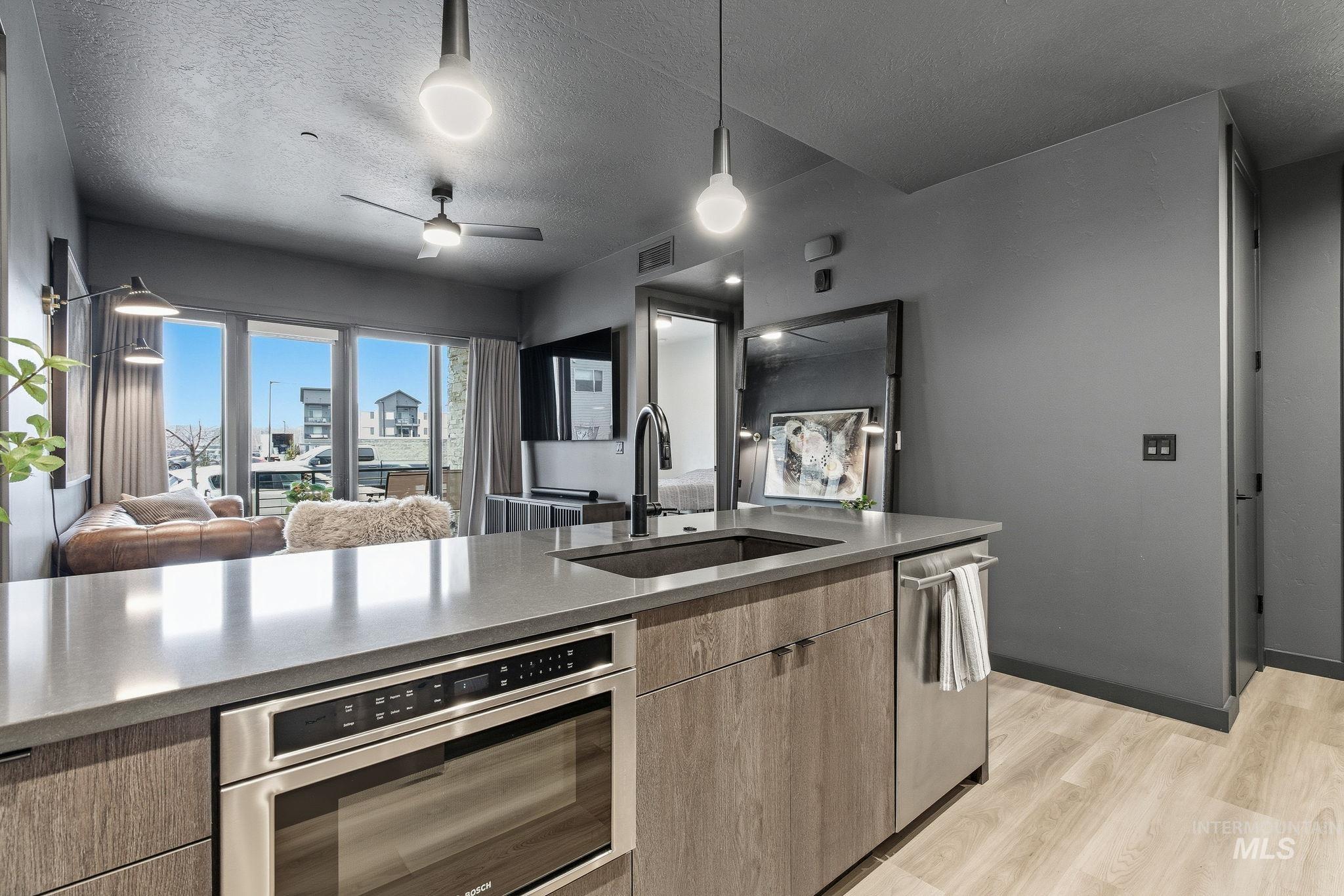 Kitchen featuring open floor plan, pendant lighting, stainless steel appliances, light wood-style flooring, and a textured ceiling