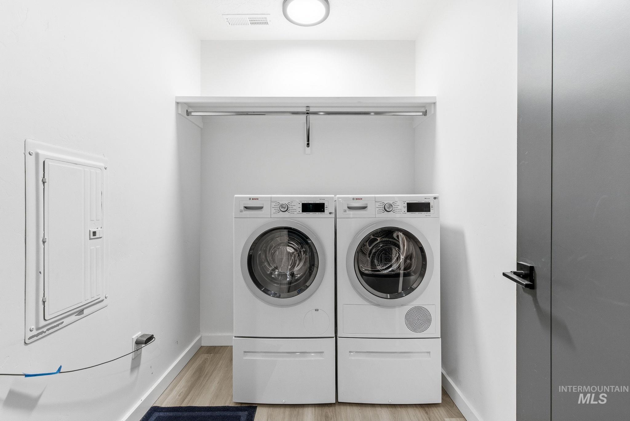 Laundry area featuring light wood-style flooring, electric panel, and washing machine and dryer