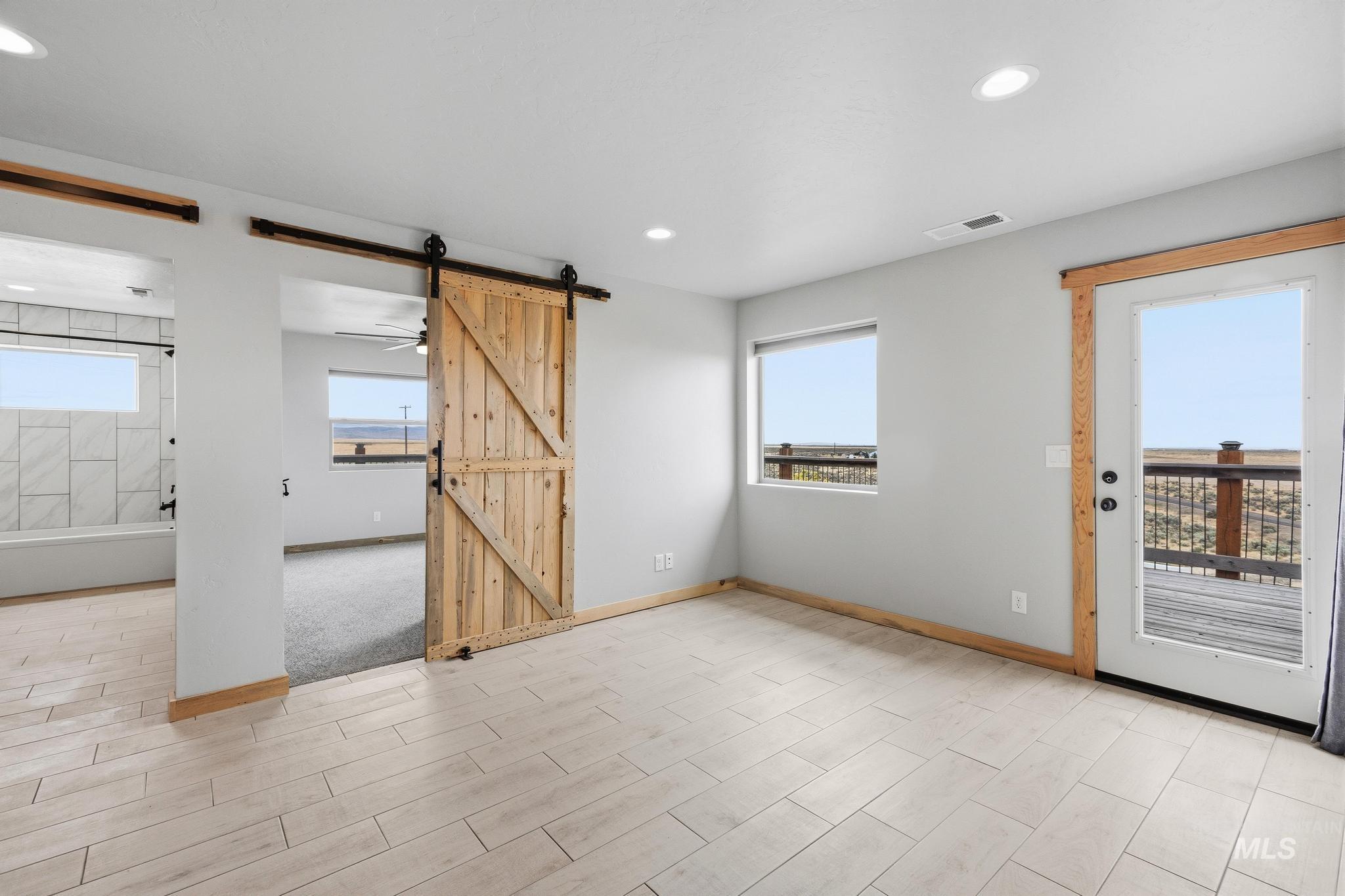 Spacious room featuring light-toned tile flooring, recessed lighting, and a barn door entry