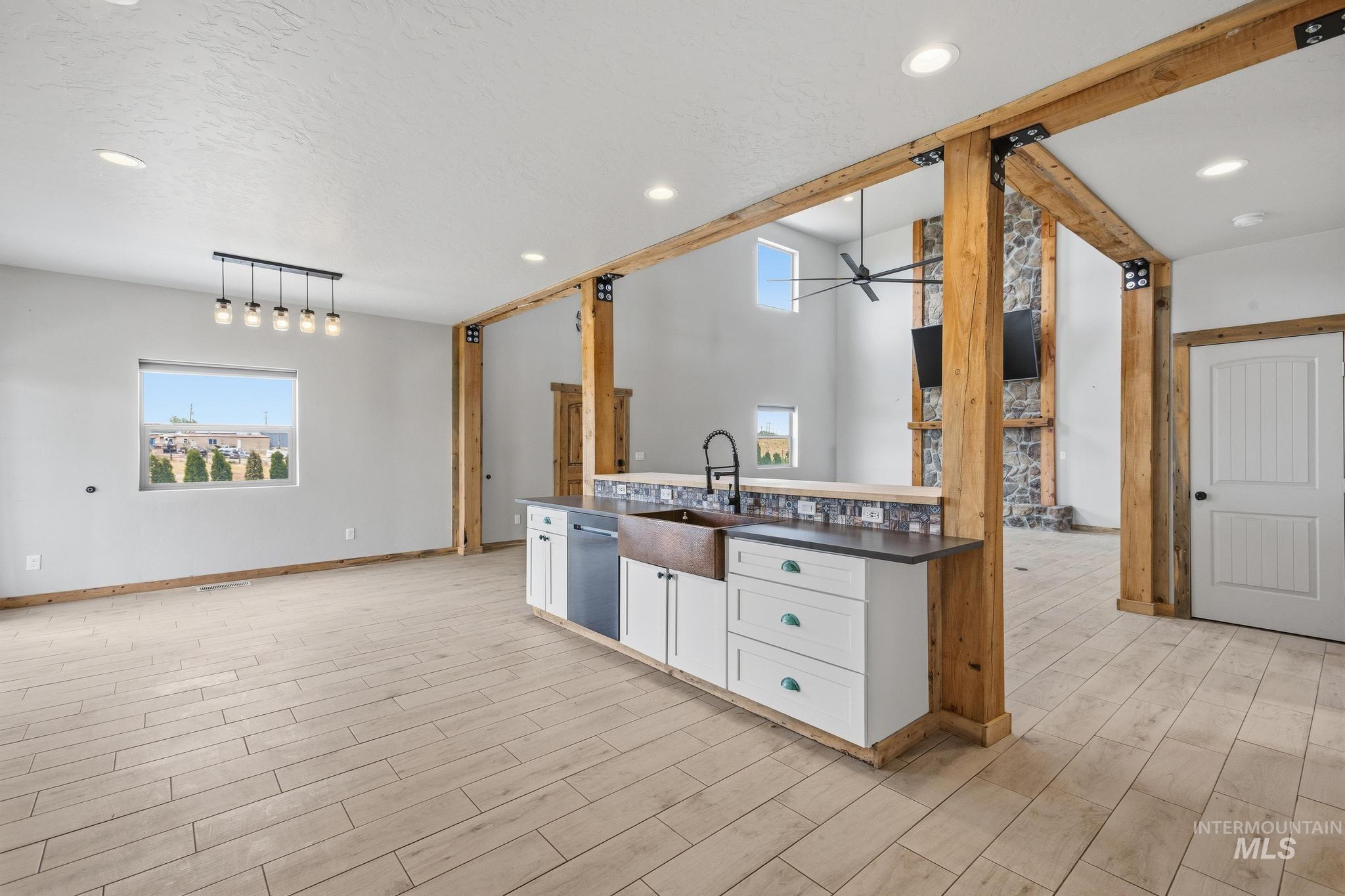 Open-concept living area featuring wood-finish tile flooring, exposed timber beams, a copper farmhouse sink, and a stone-clad fireplace