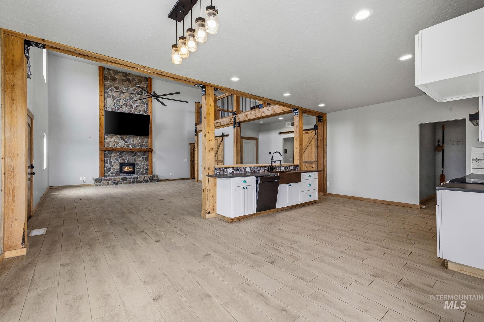 Expansive living area featuring a floor-to-ceiling stone fireplace, high ceilings, wood-finish flooring, and exposed wood beam accents