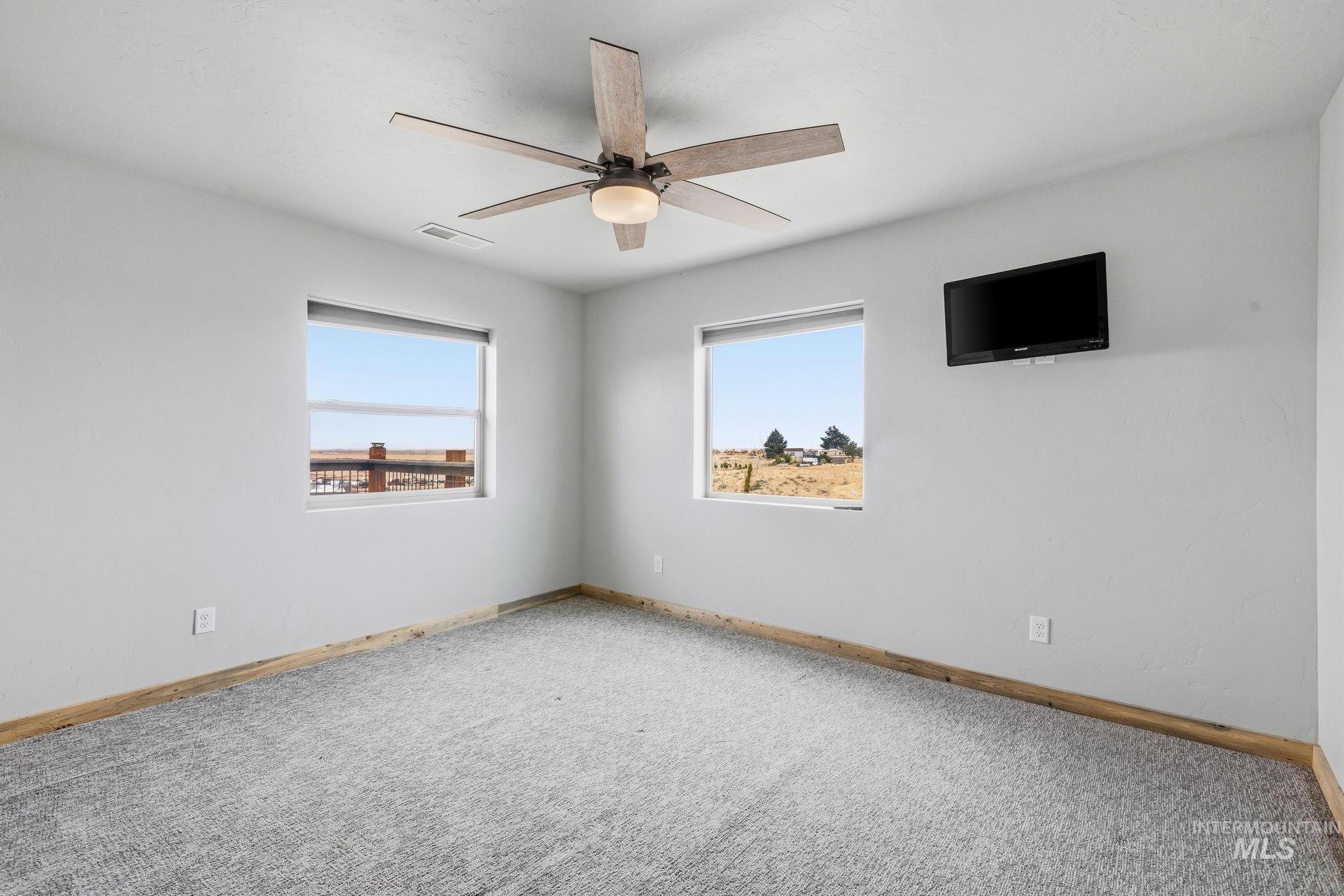Spacious room featuring light gray walls, textured gray carpeting, and a wood-finish baseboard trim