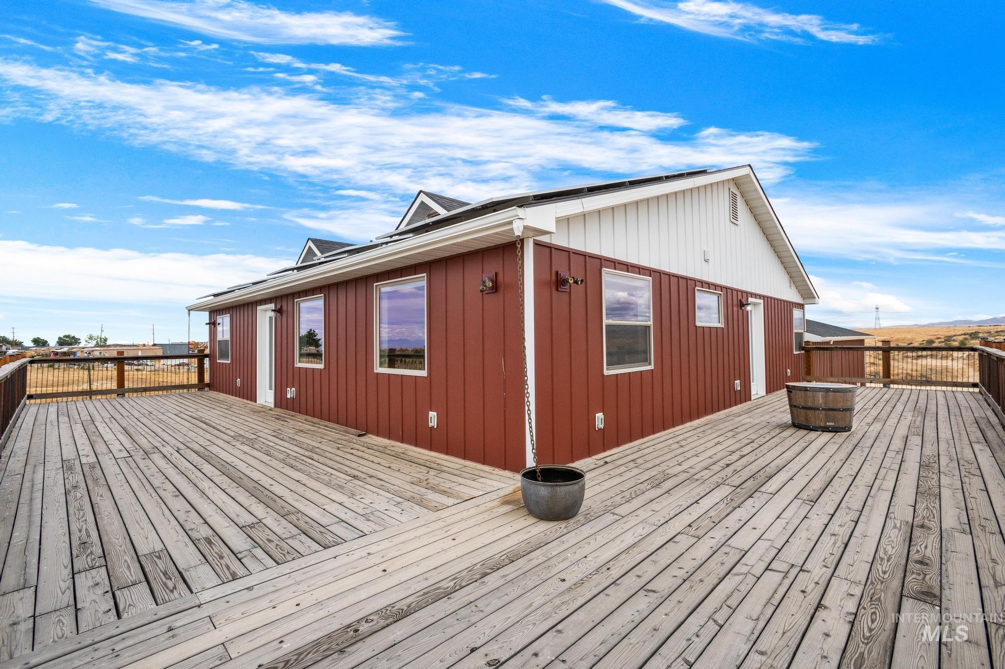 Expansive outdoor decking features a natural wood finish, a perimeter railing, and direct access to the red vertical siding exterior of the home