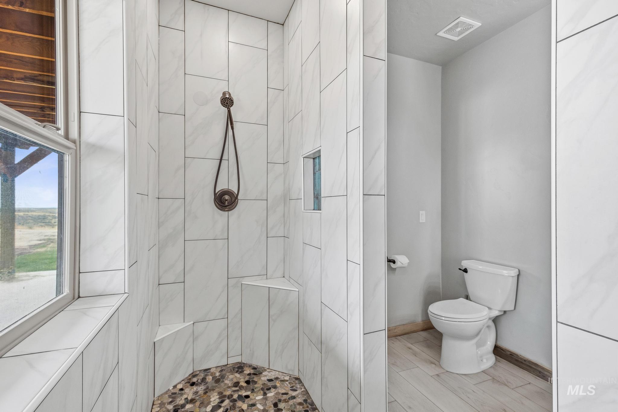 Spacious shower featuring white subway tile, a built-in bench, a mosaic tile floor, and an integrated shower niche
