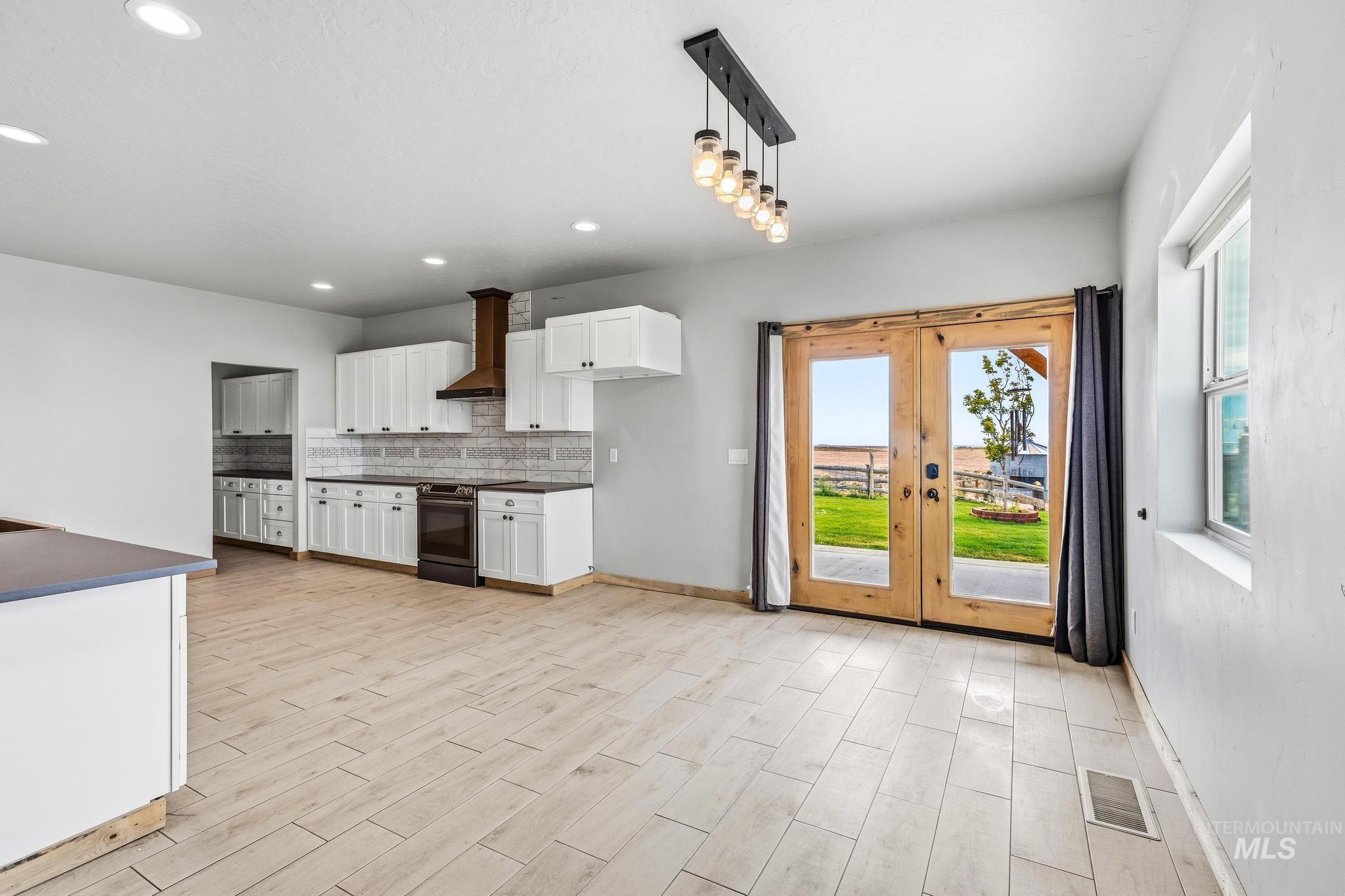 Open-concept kitchen with white cabinetry, a wood-finish range hood, and a dark tile backsplash
