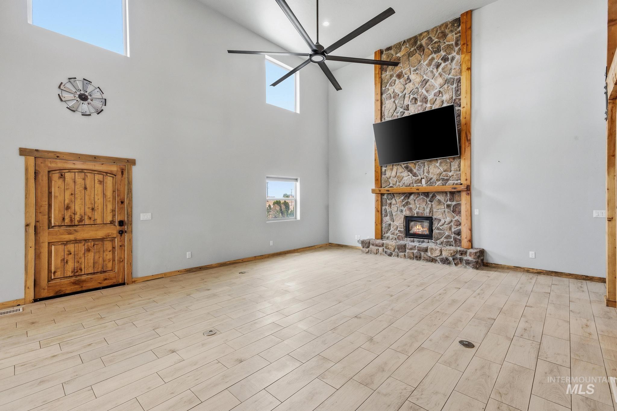Spacious living area featuring a floor-to-ceiling stone fireplace, soaring ceilings, and natural wood-finish flooring