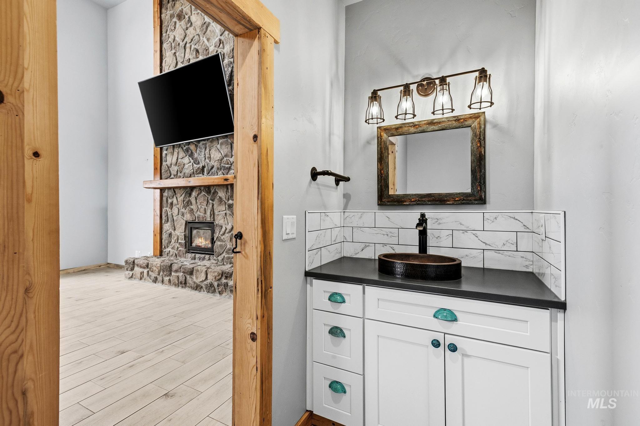 White vanity with a vessel sink, dark countertop, and tile backsplash