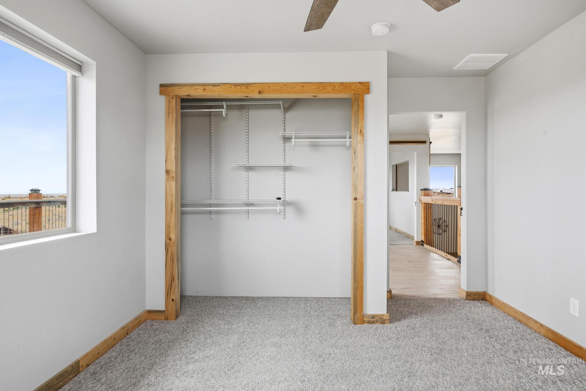 Bedroom featuring light gray carpeting, a window with a distant landscape, and a closet with a natural wood-trimmed opening and built-in metal shelving