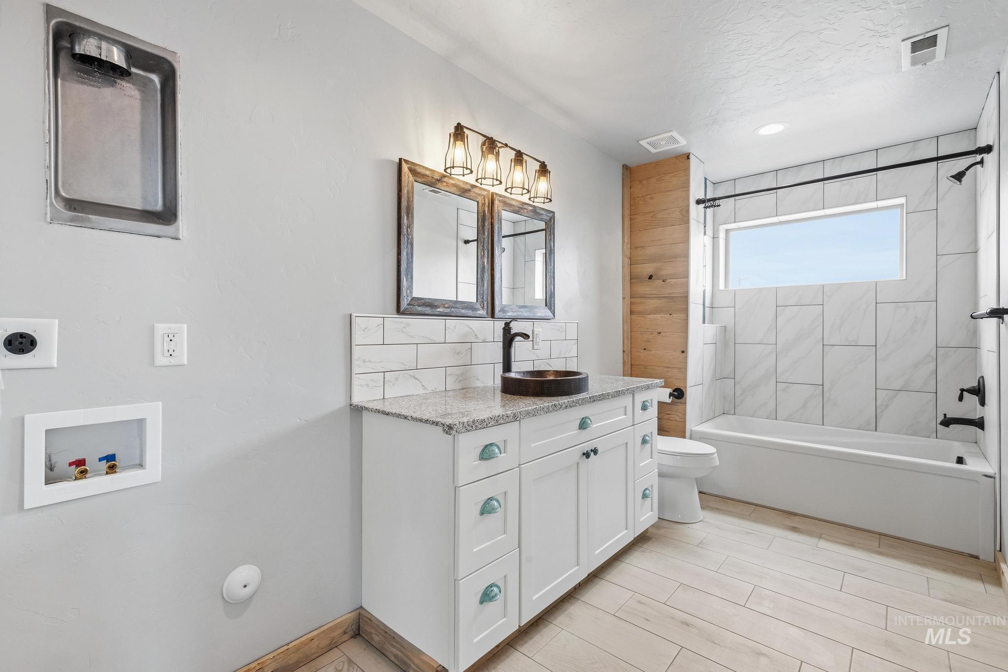 Full bathroom featuring a white vanity with a stone countertop, vessel sink, and industrial-style lighting