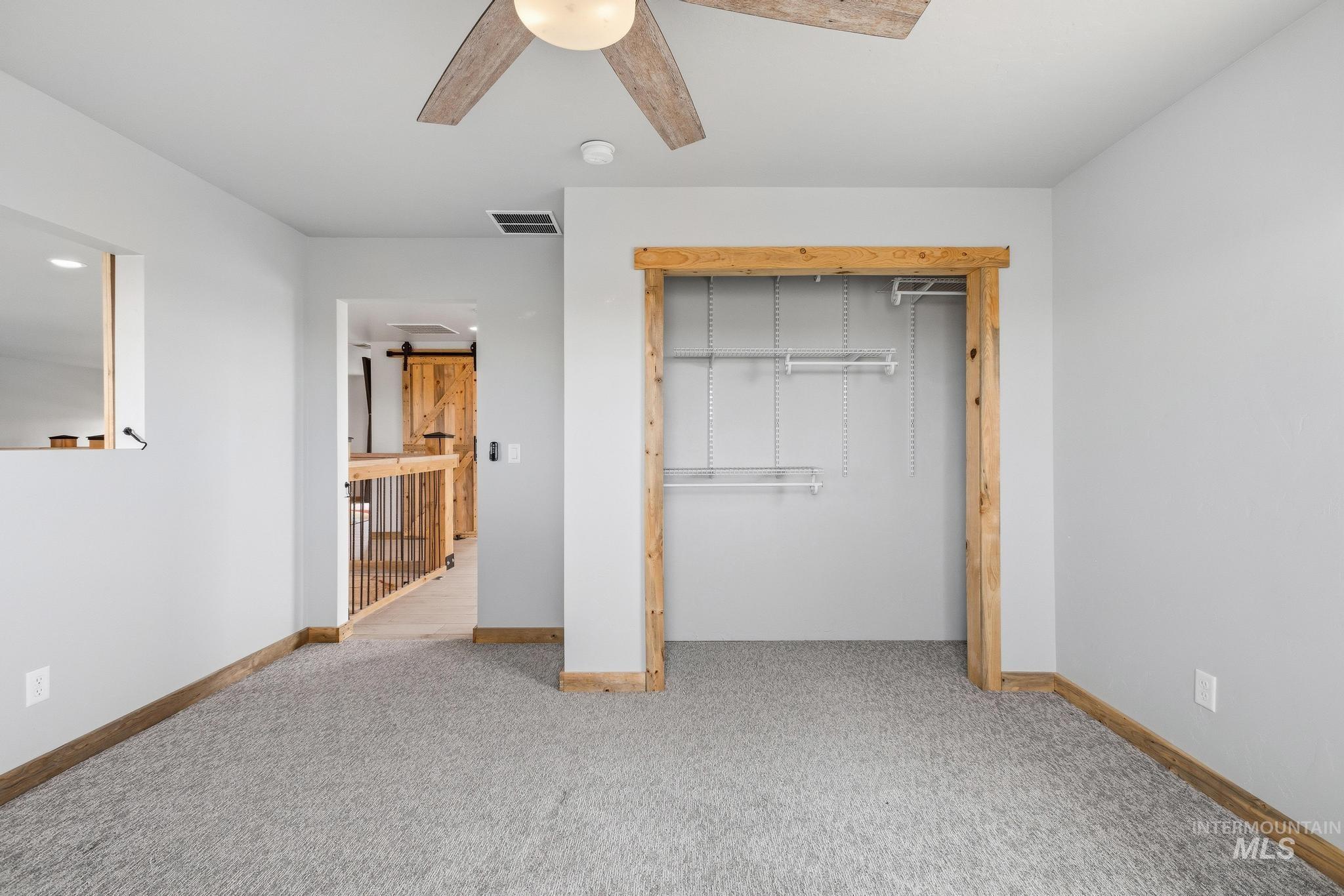 Carpeted room featuring a ceiling fan with light fixture, built-in closet with shelving and hanging rods, and wood-finish trim
