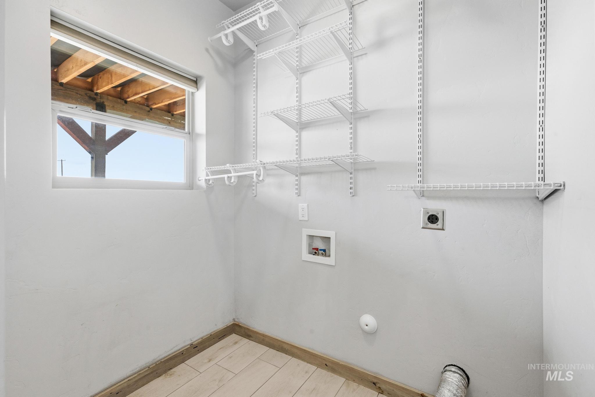 Dedicated utility space featuring a window, built-in wire shelving, and wood-finish flooring