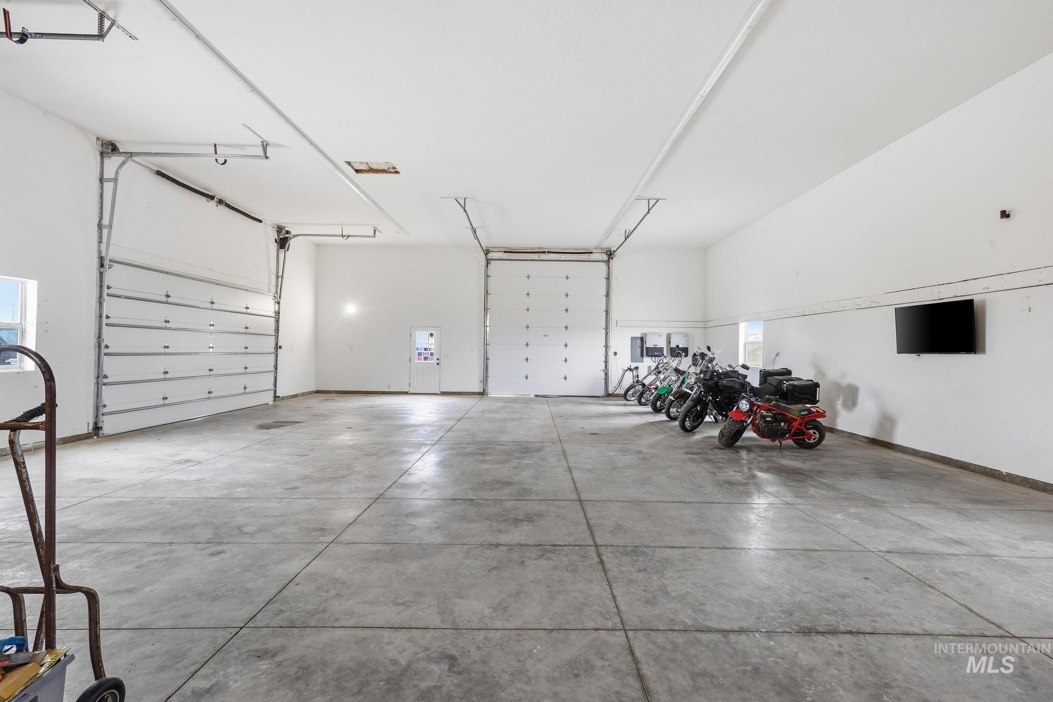 Spacious garage featuring a concrete floor, multiple overhead doors, high ceilings, and white painted walls