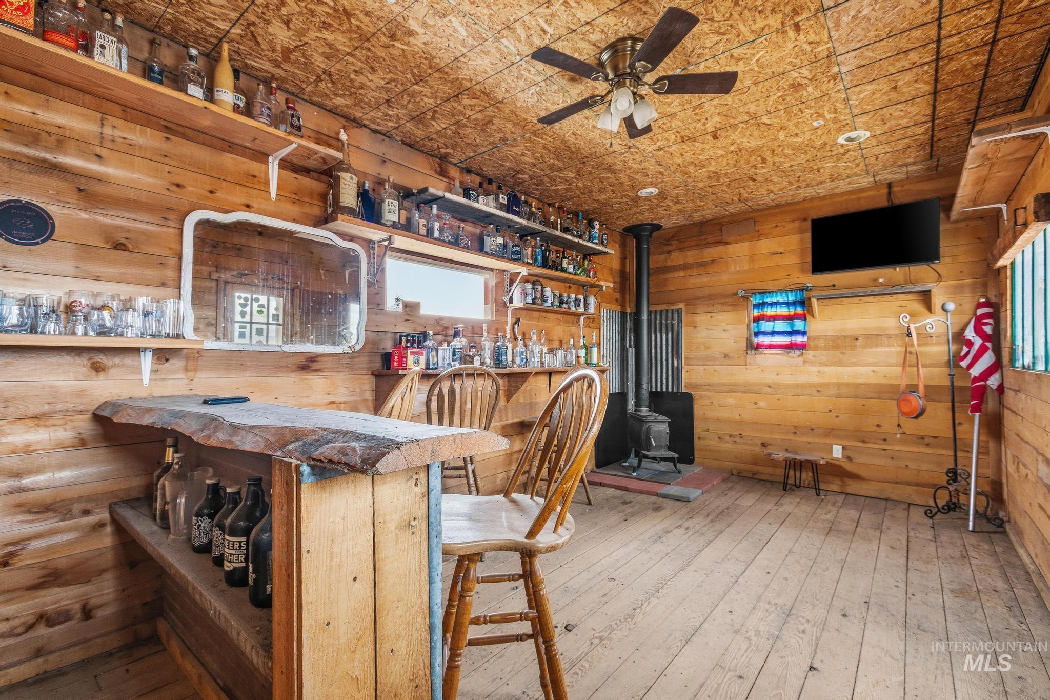 Wood-paneled room featuring a live-edge wooden bar with shelving, a freestanding wood-burning stove, and a ceiling fan