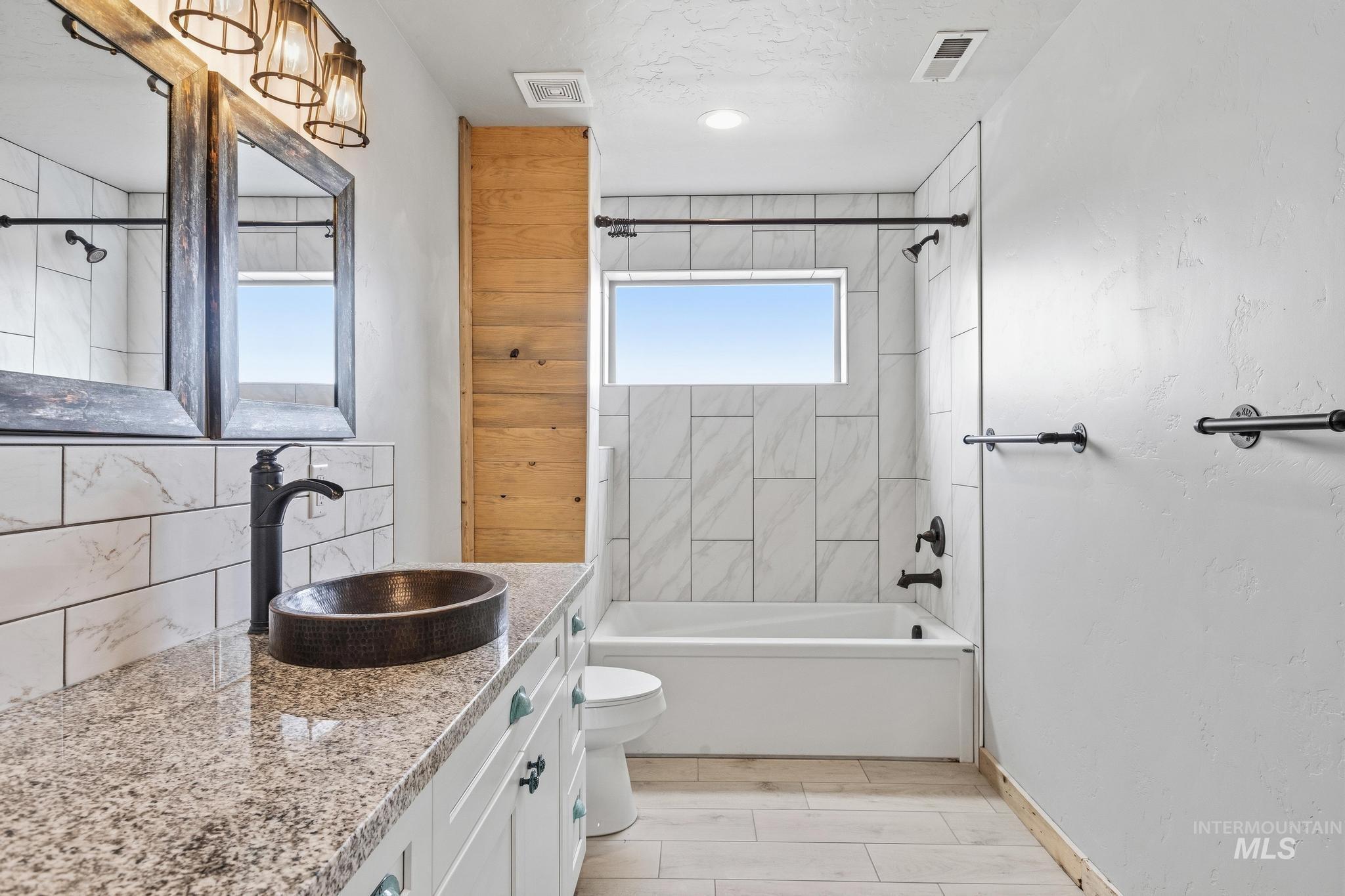 Bathroom featuring a granite-look countertop with a vessel sink, white subway tile backsplash, and wood-finish accent wall