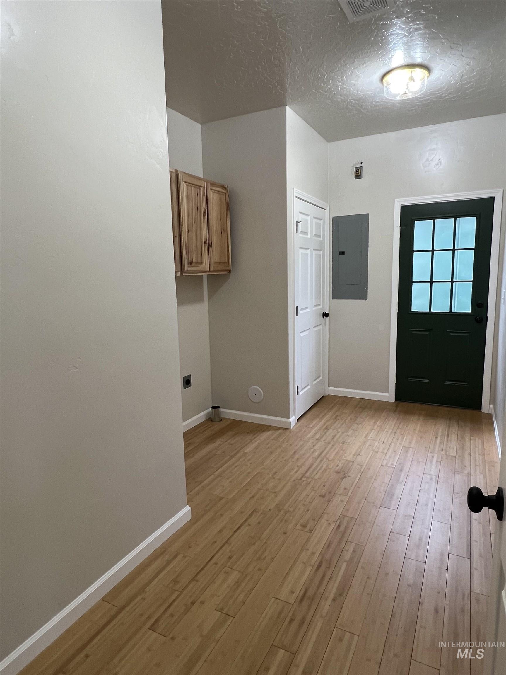 Laundry area with electric panel, light wood-type flooring, a textured ceiling, and cabinet space