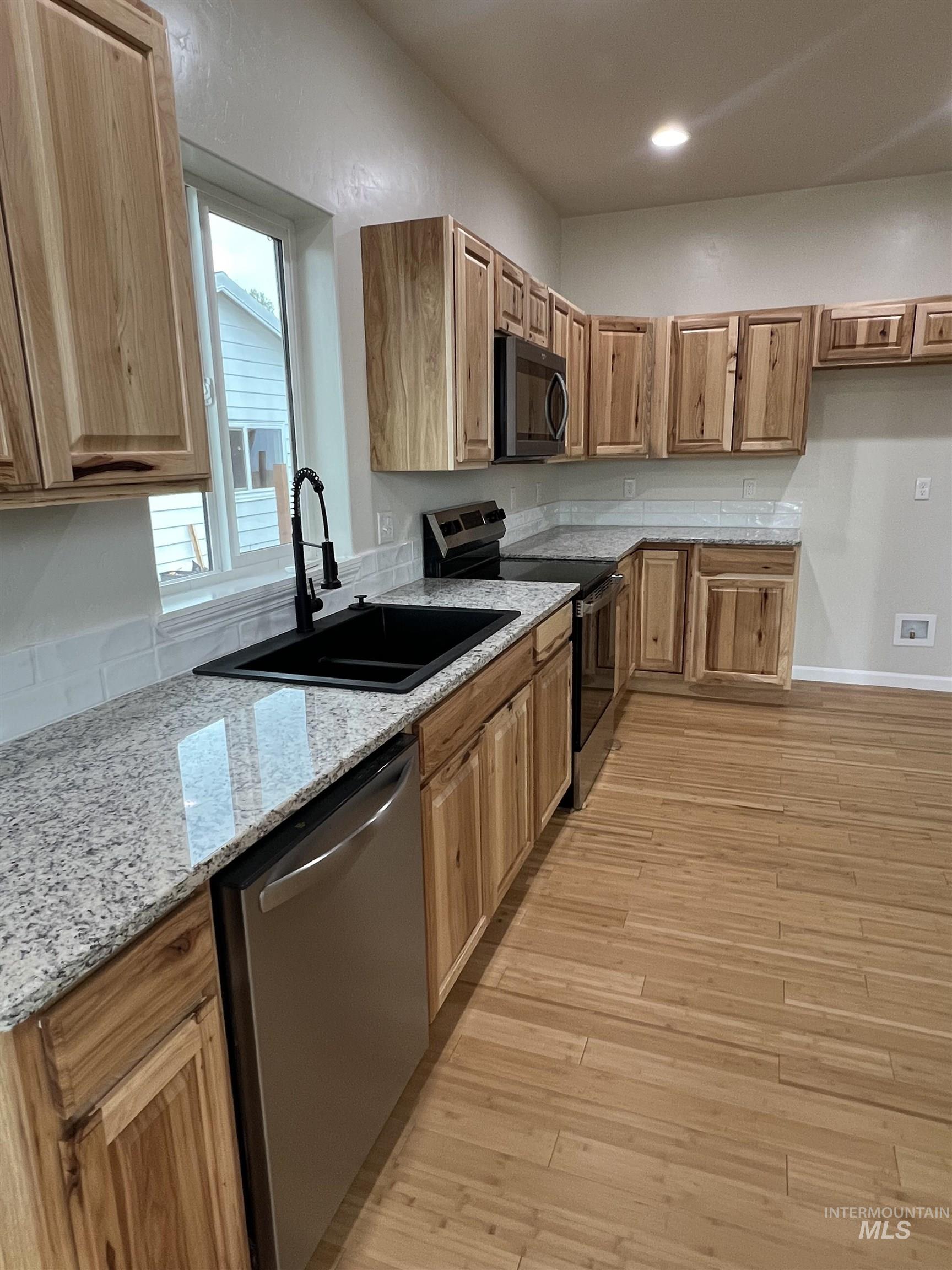 Kitchen with stainless steel appliances, light wood-type flooring, light stone counters, brown cabinetry, and recessed lighting