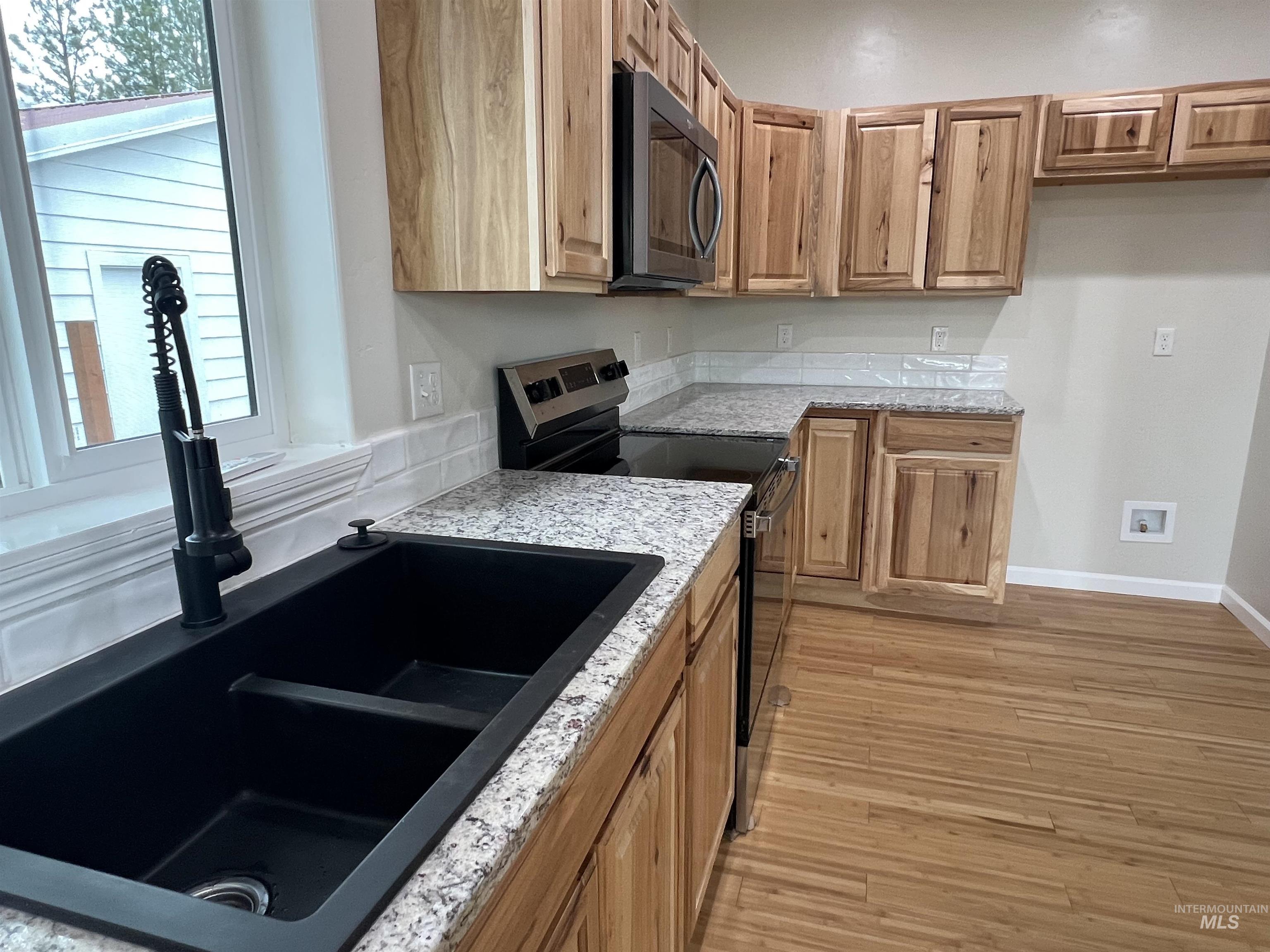Kitchen with black appliances, plenty of natural light, light wood finished floors, and light stone countertops