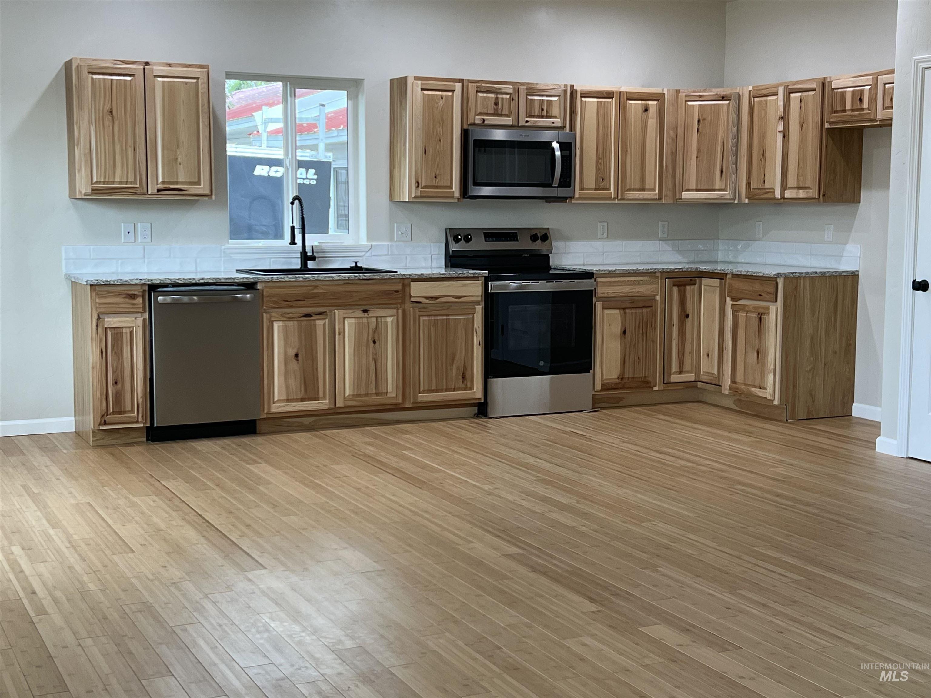 Kitchen featuring appliances with stainless steel finishes, light wood finished floors, light stone countertops, and brown cabinetry