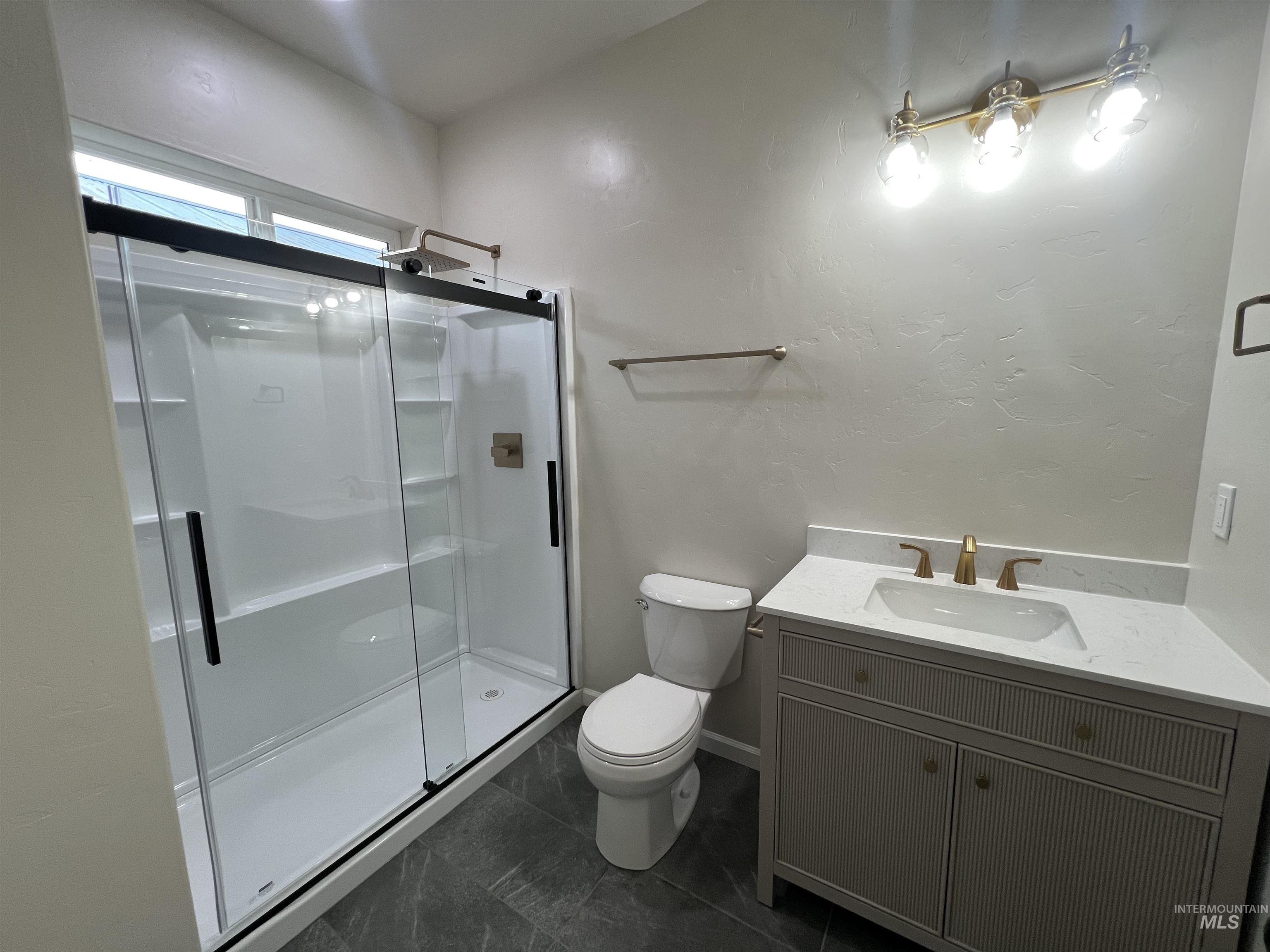 Bathroom featuring vanity, a stall shower, a textured wall, and dark tile patterned flooring