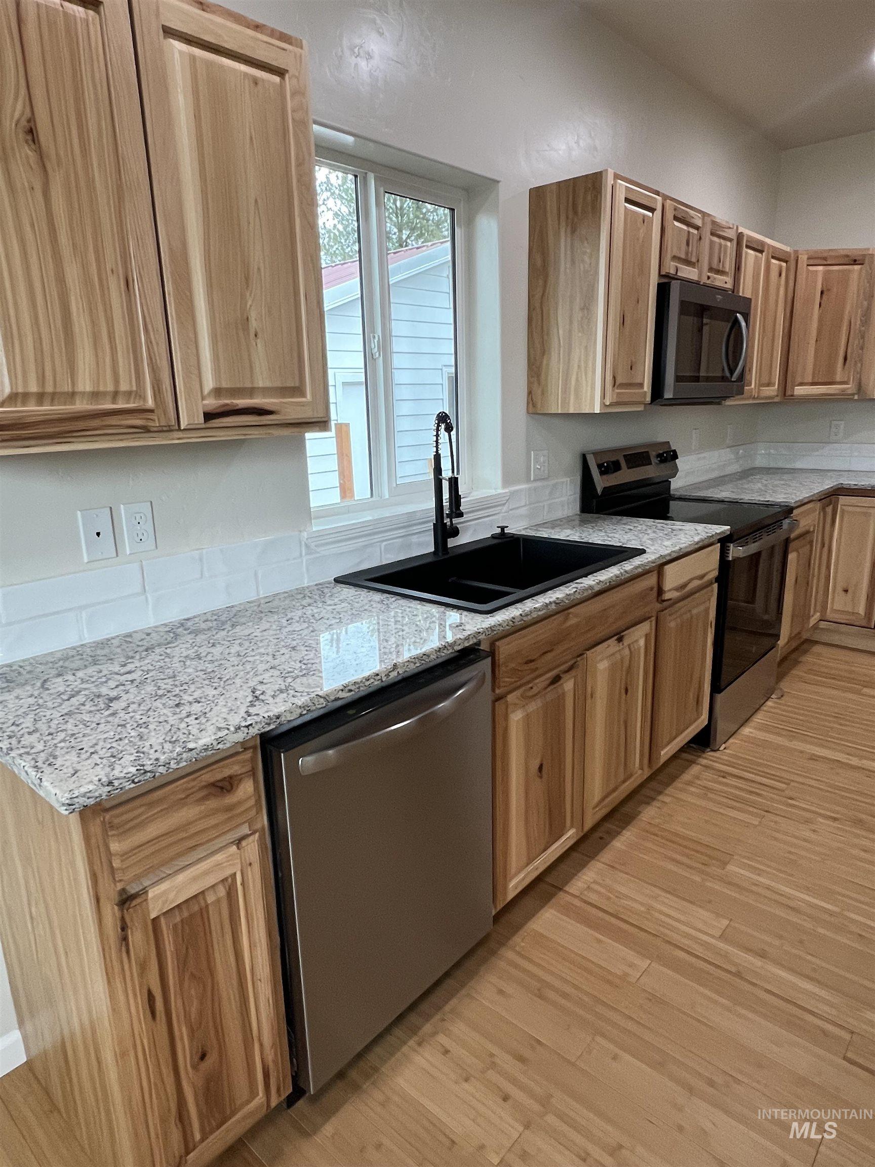 Kitchen featuring appliances with stainless steel finishes, light stone countertops, and light wood-style floors