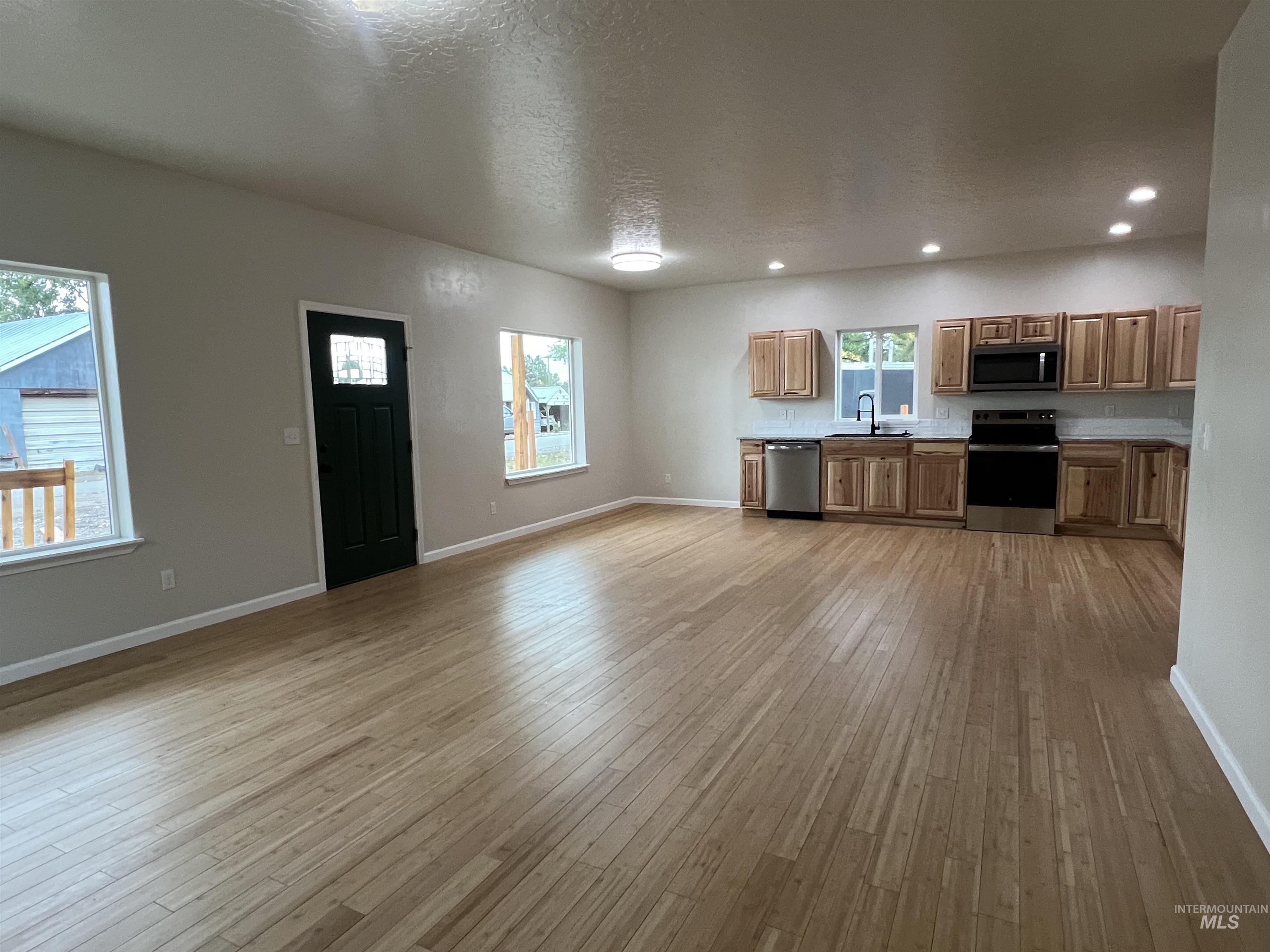 Kitchen featuring appliances with stainless steel finishes, brown cabinets, a textured ceiling, light countertops, and light wood-type flooring