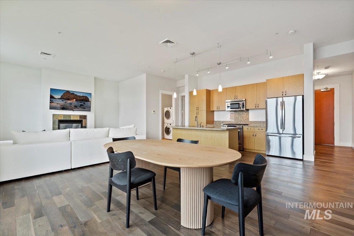 Kitchen with stainless steel appliances, decorative light fixtures, a kitchen island with sink, open floor plan, and dark wood-style floors